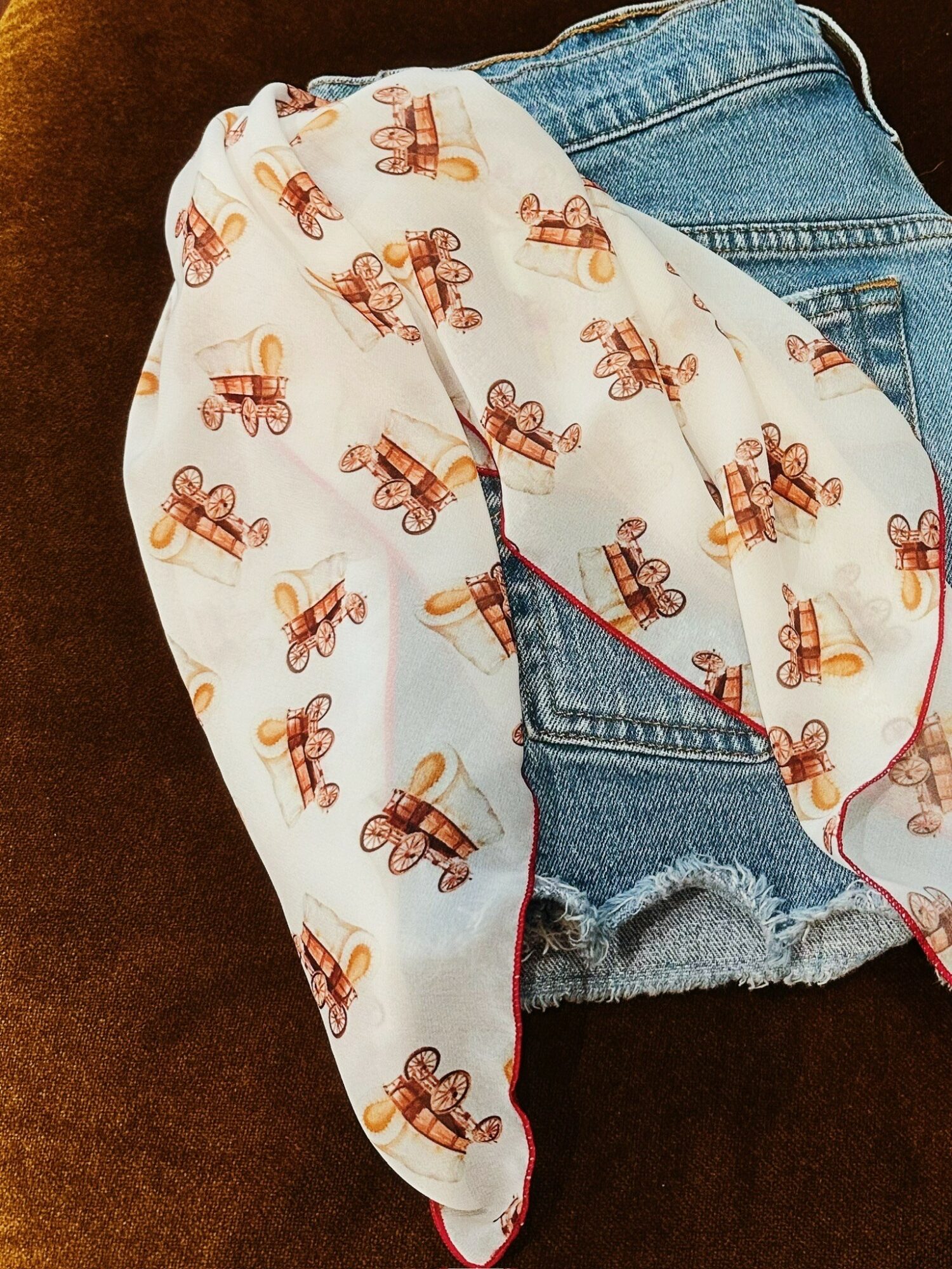 A white fabric with a pattern of small brown and orange bicycles, draped over blue denim shorts with frayed edges.