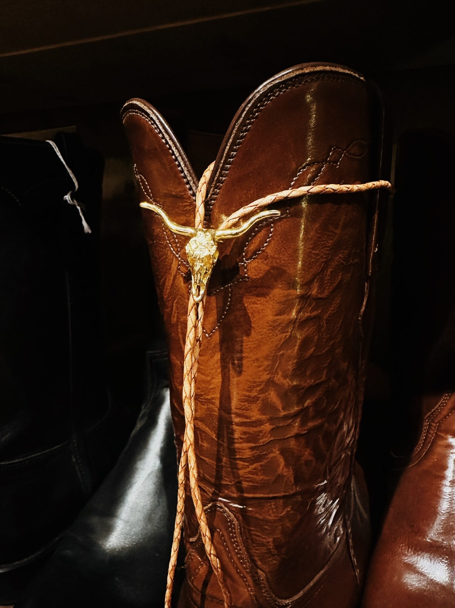 A tall brown leather cowboy boot with a decorative rope tied around the top, against a dark background.