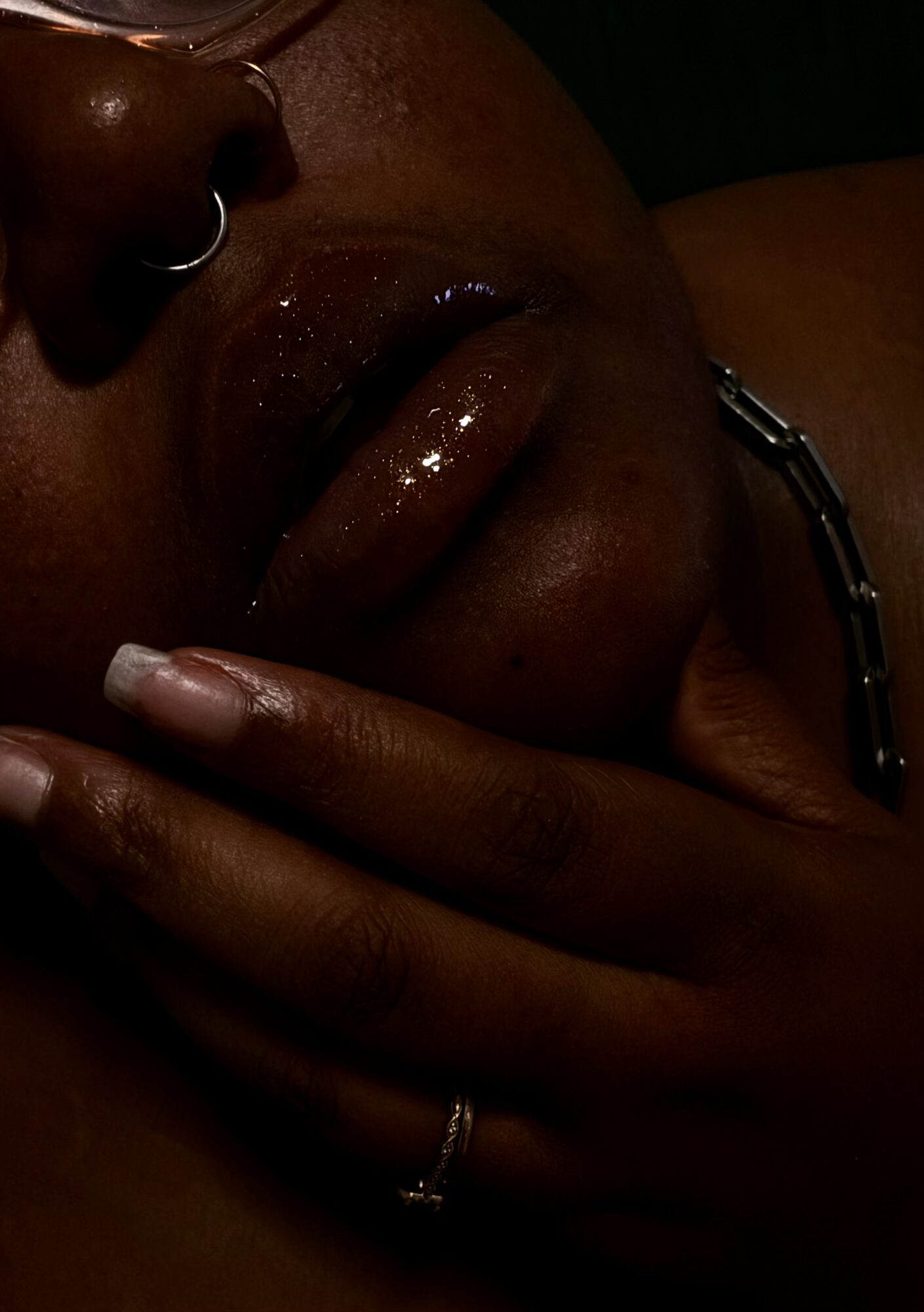 Close-up of a person's face with lips slightly parted, hand resting near chin, dark skin, jewelry visible.
