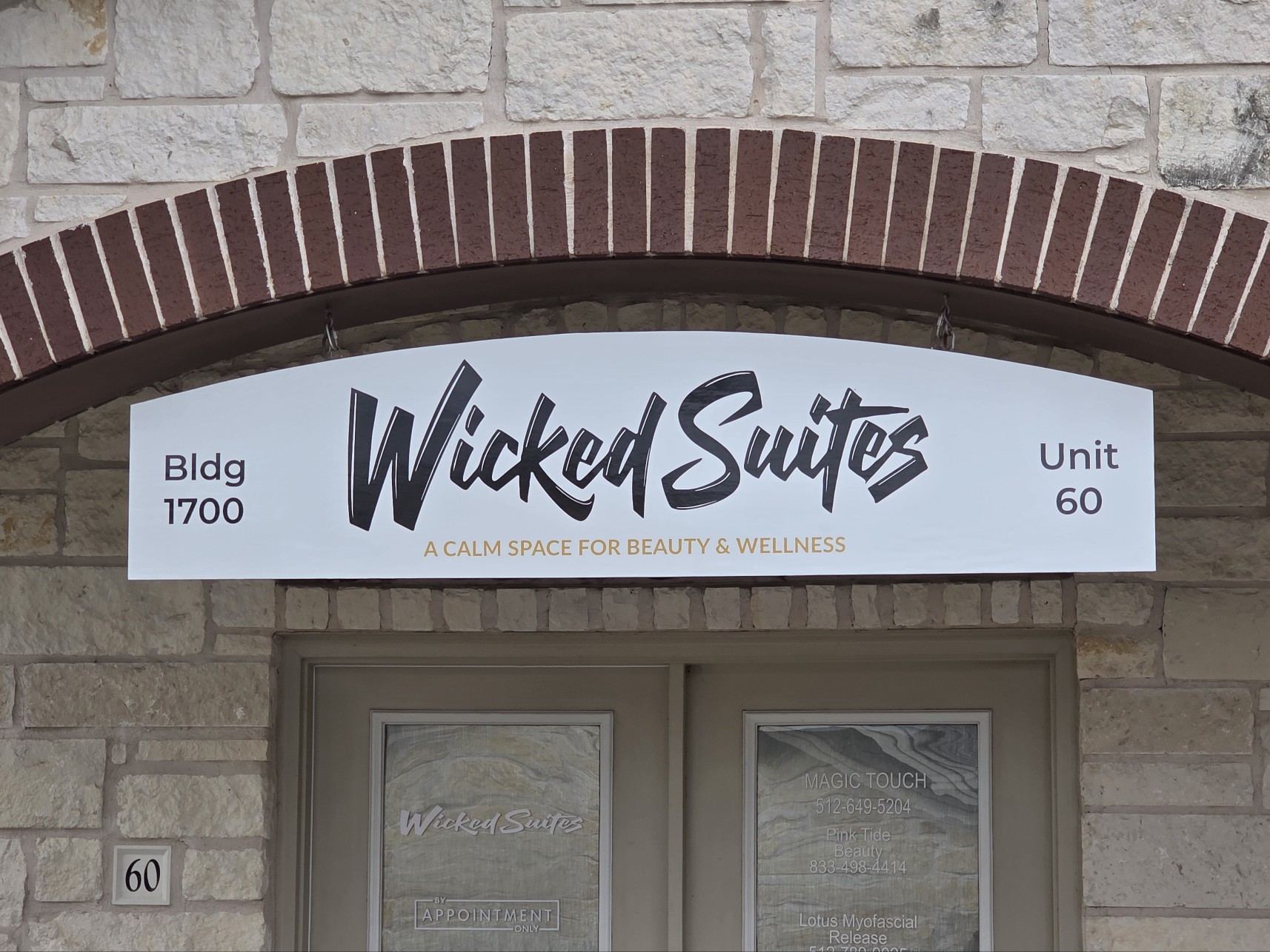 Sign for Wicked Suites, a beauty and wellness space, with building number 1700 and unit 60, mounted above a door.