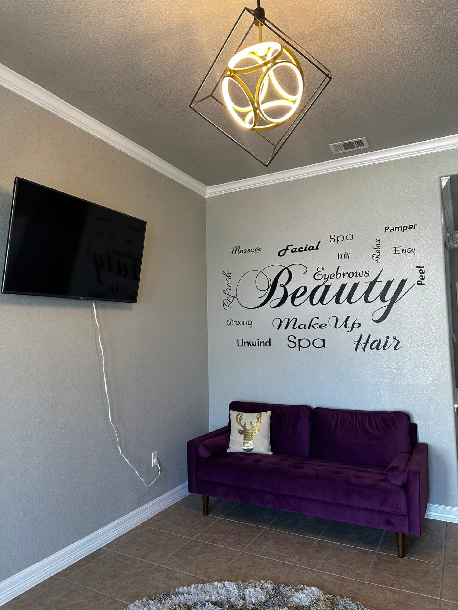 Living room corner with wall decor, purple sofa, and wall-mounted TV, ceiling light fixture, and a small pillow on the sofa.