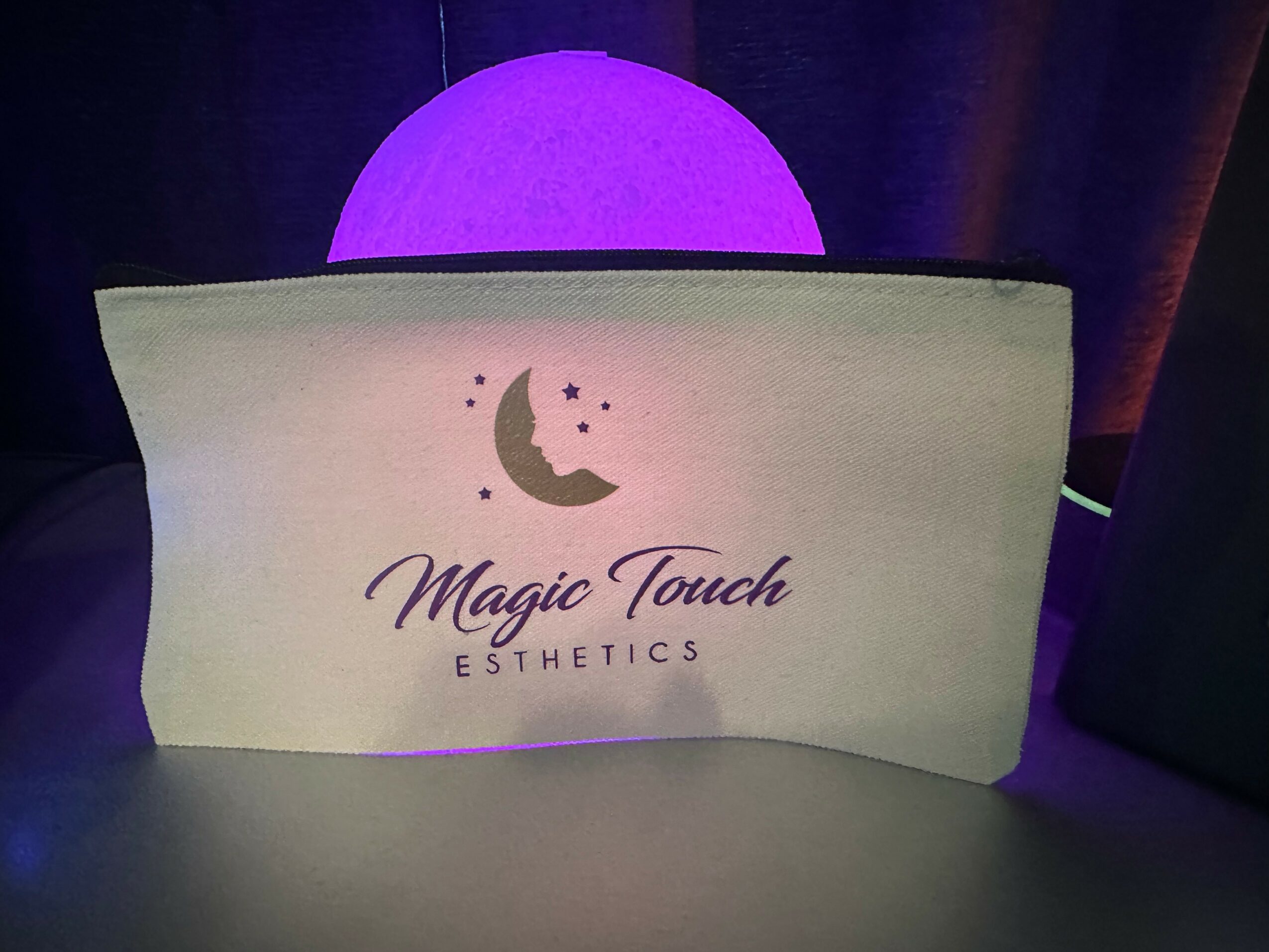 A sign with a moon and stars, reading 'Magic Touch ESTHETICS', in front of a glowing purple sphere.