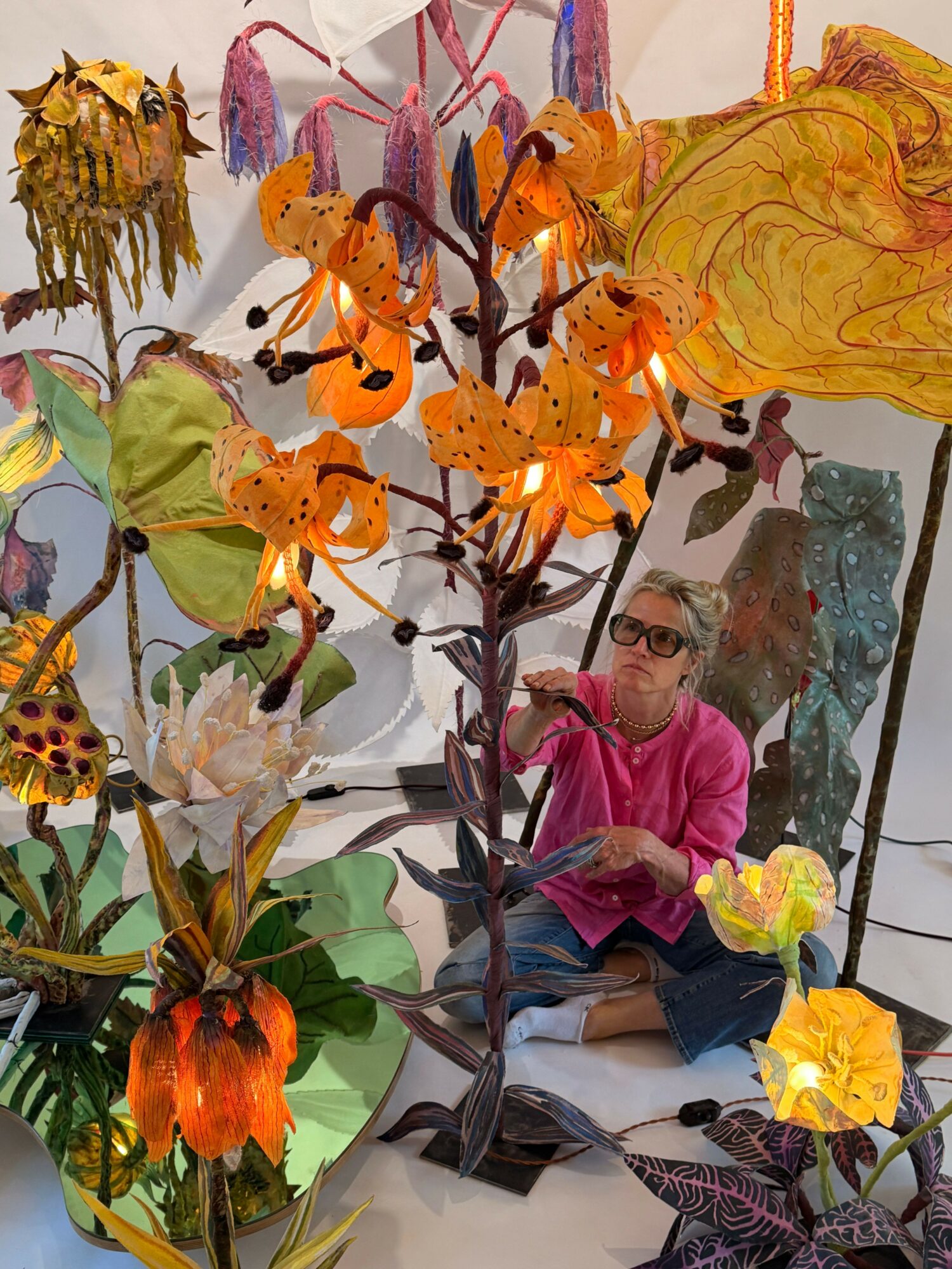 Display of colorful artificial flowers and butterflies with a person in pink in the background.