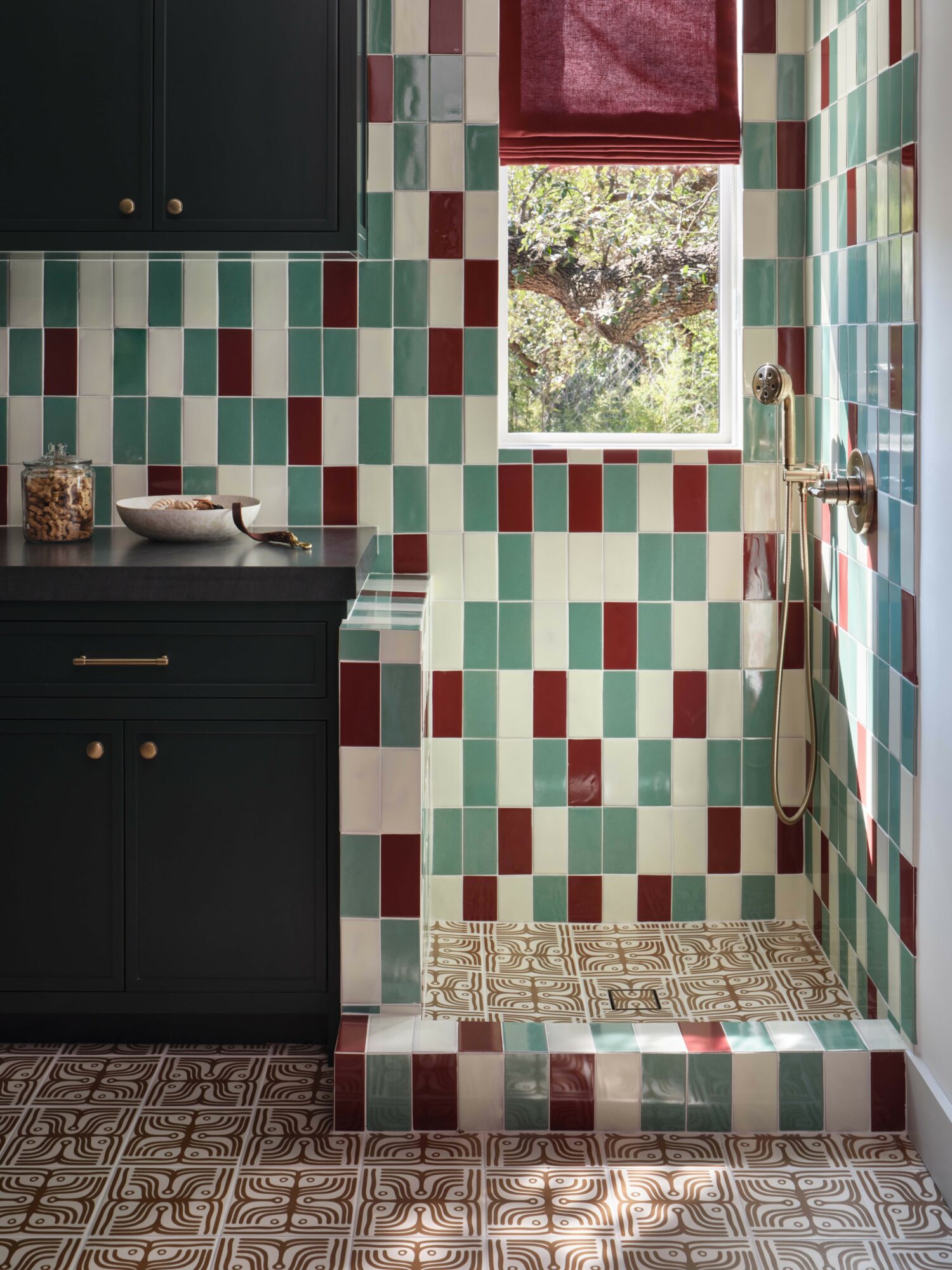 Kitchen corner with colorful tiled walls, a window with a red curtain, dark cabinets, and patterned floor tiles.