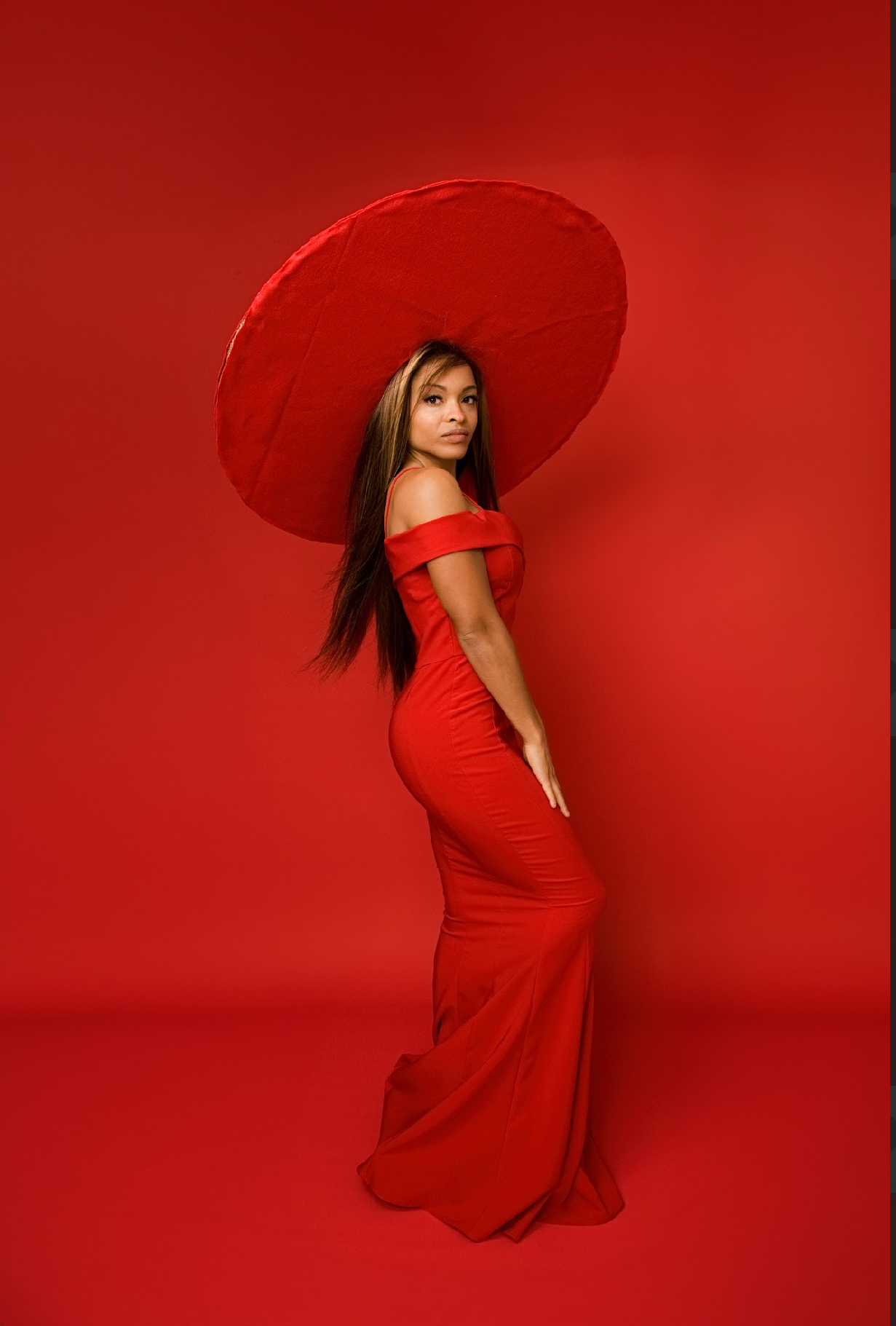 Woman in red dress holding a large red umbrella against a red background, looking over her shoulder.