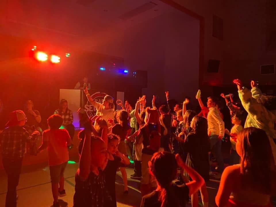 People dancing and enjoying a party with colorful lights in a dark indoor space.