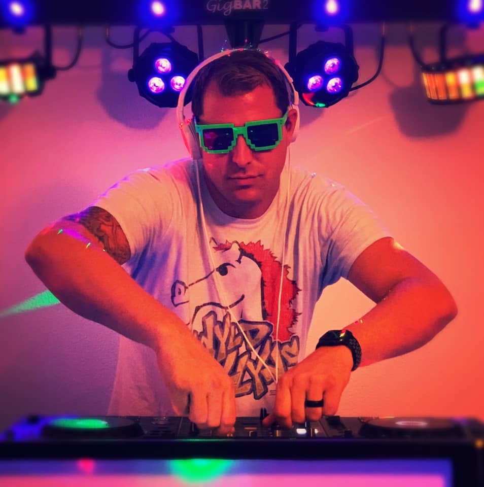 Person wearing sunglasses and headphones, DJing with colorful lights in background.