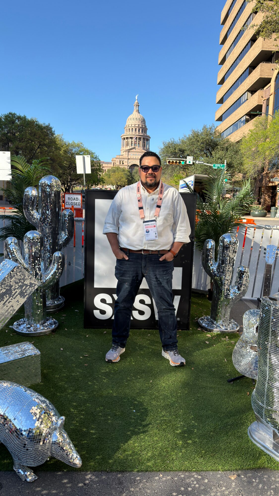 Man standing outdoors with Texas-shaped reflective sculptures, Texas State Capitol in background, clear blue sky.