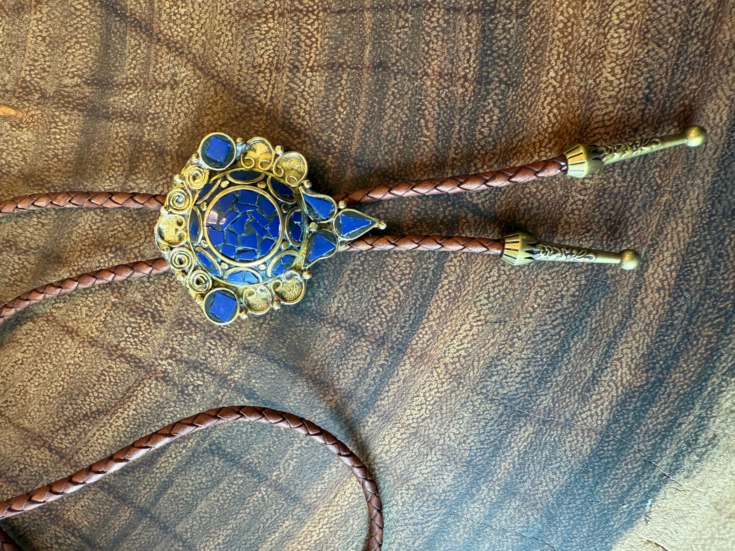 Ornate gold and blue decorative object with two dangling gold and blue elements on a textured fabric background.