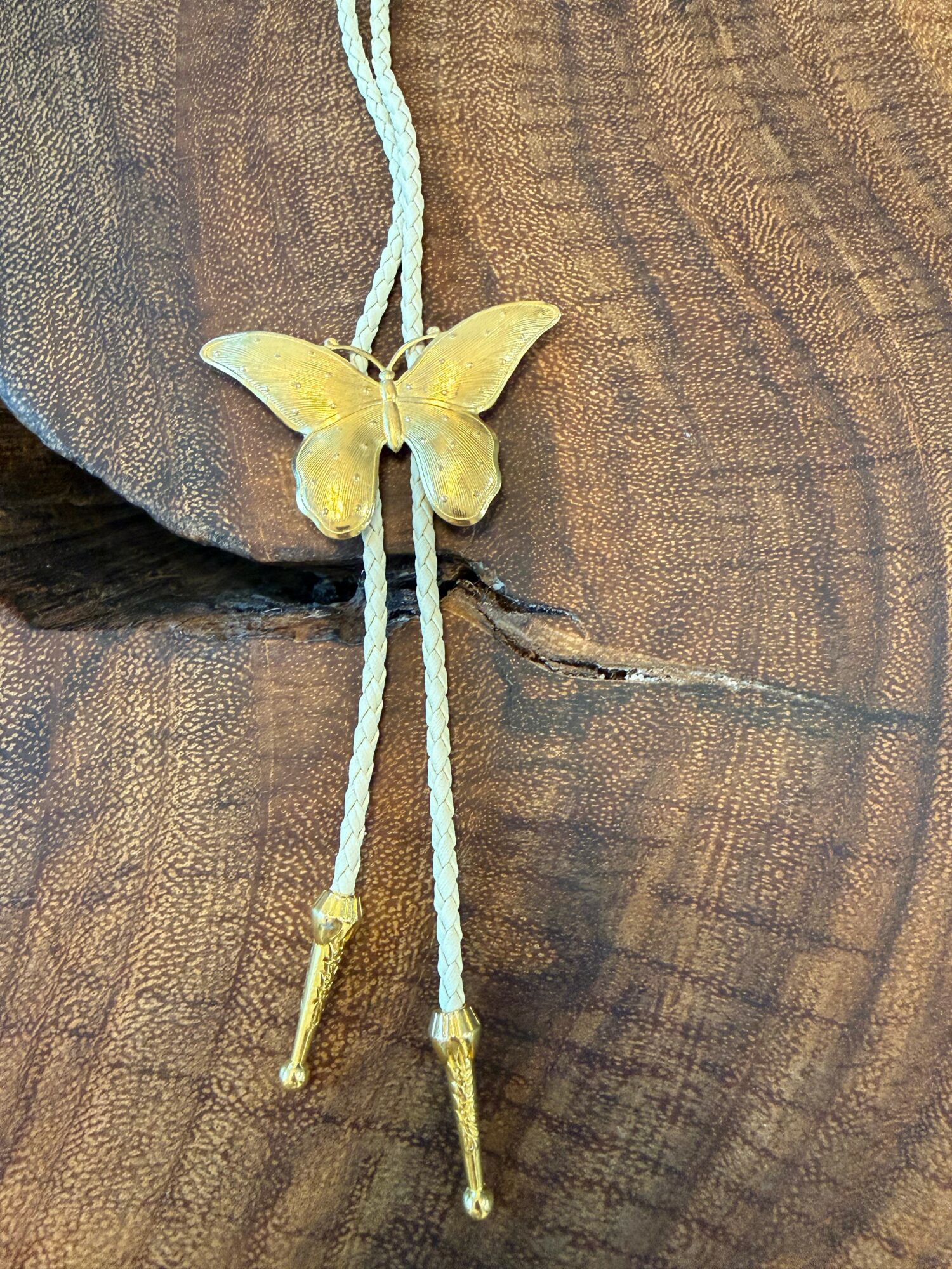 Yellow butterfly-shaped pendant with two cords hanging down, on a wooden surface.