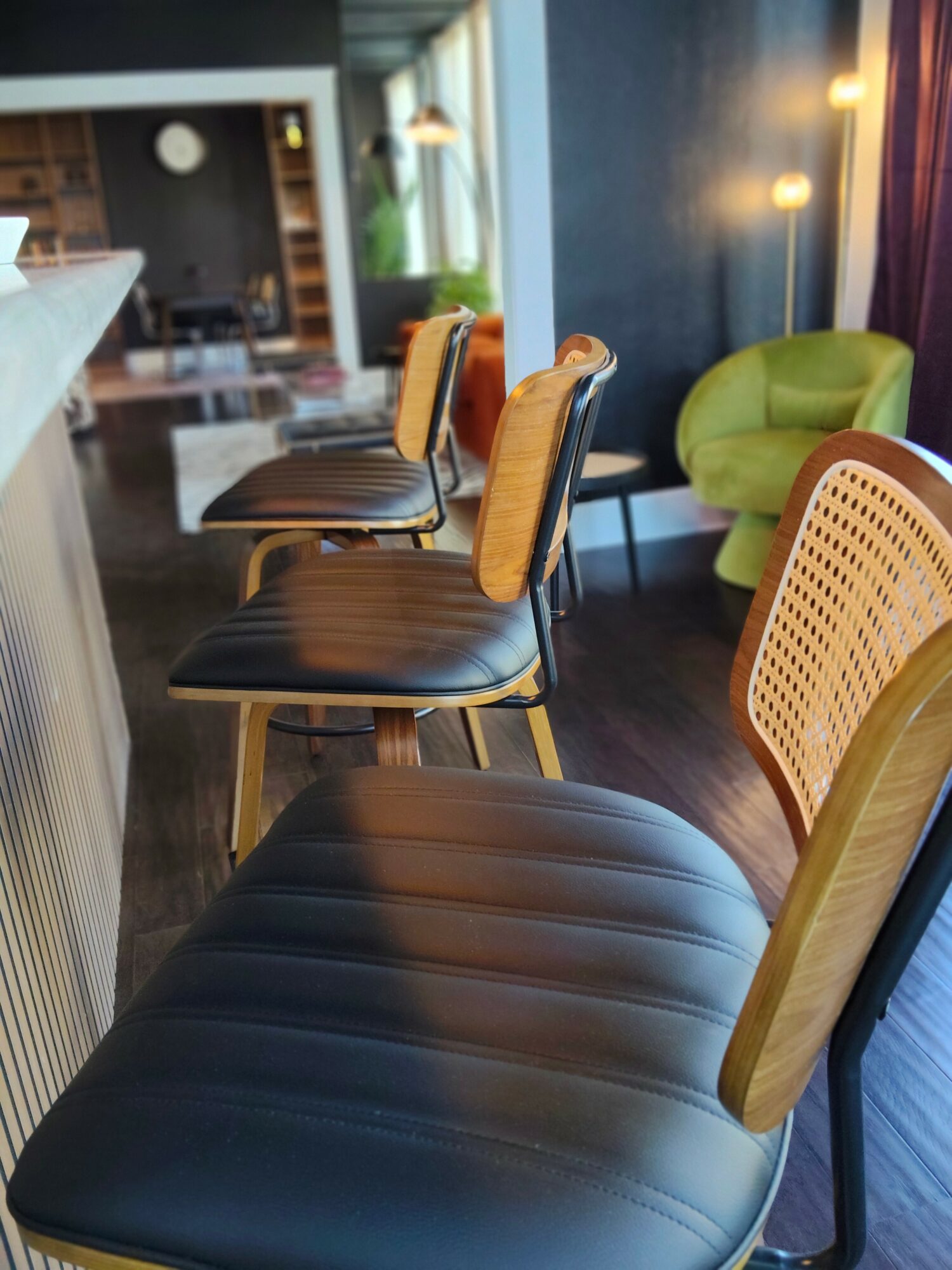Row of chairs with black seats and wooden backs in a modern interior space, with a green armchair nearby.