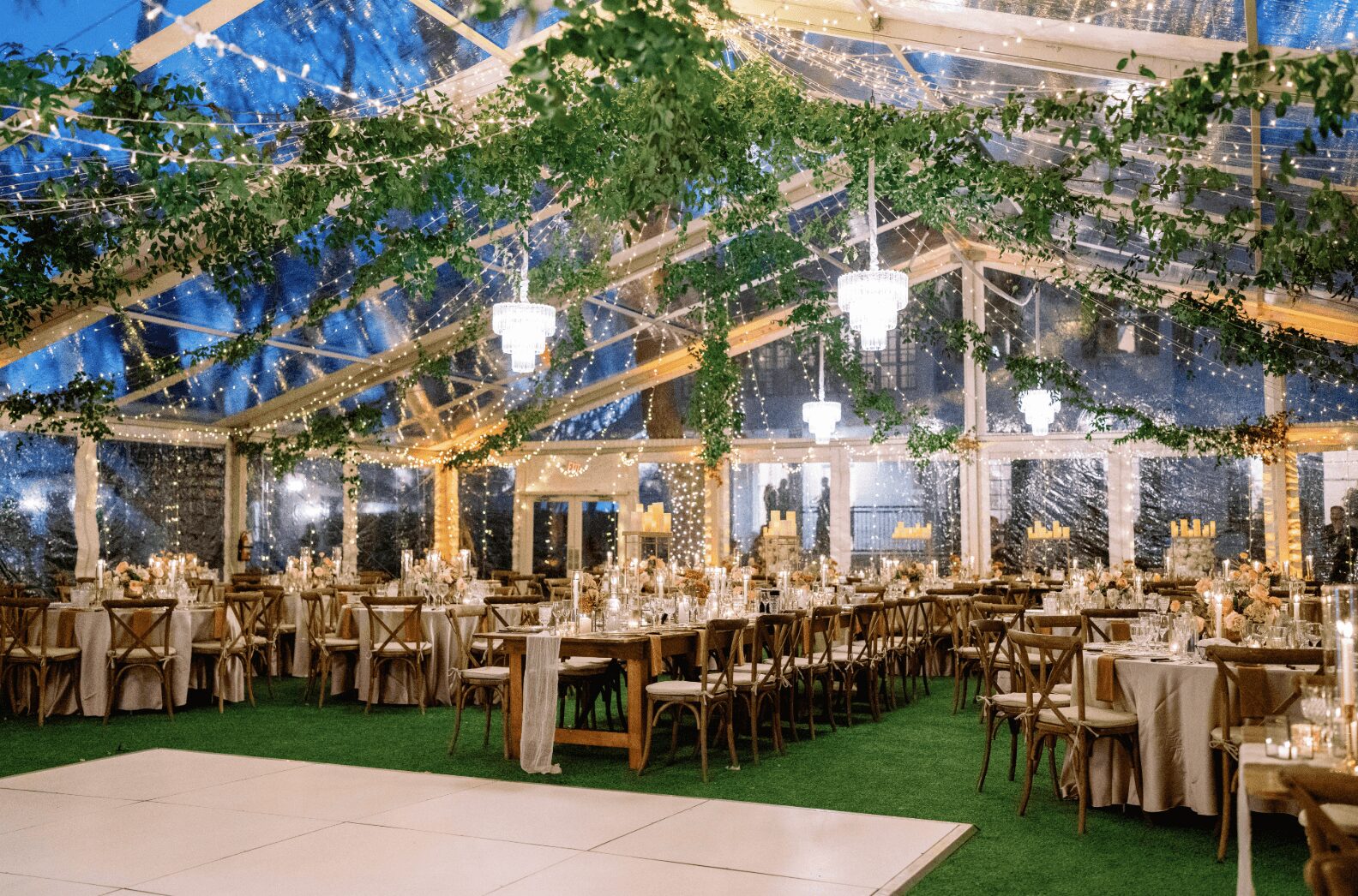 Indoor event space decorated with string lights, tables with chairs, and greenery, set for a celebration or banquet.