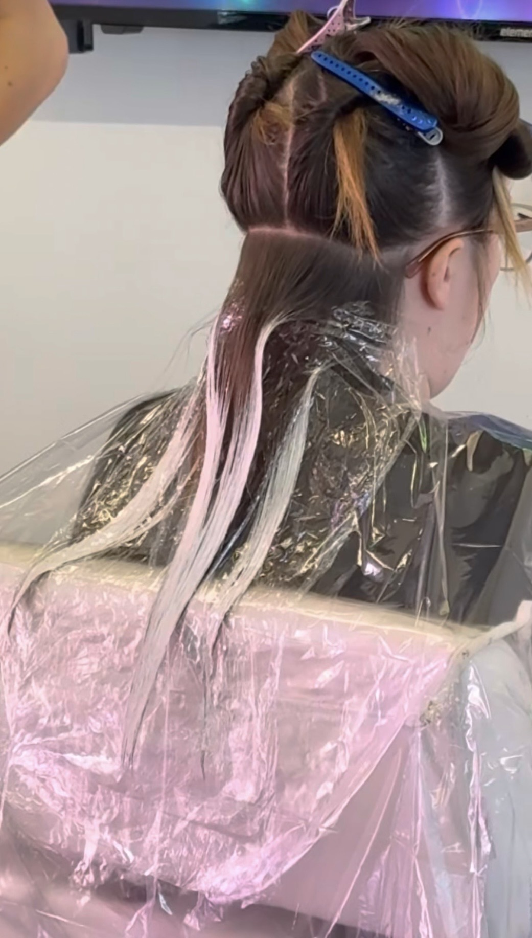 Person getting hair dyed with pink color, hair sectioned and covered with foil, in salon setting.