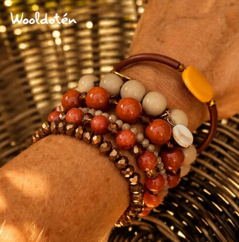 Multiple beaded bracelets on a person's wrist, with a woven background, some beads are white and others are reddish-brown.