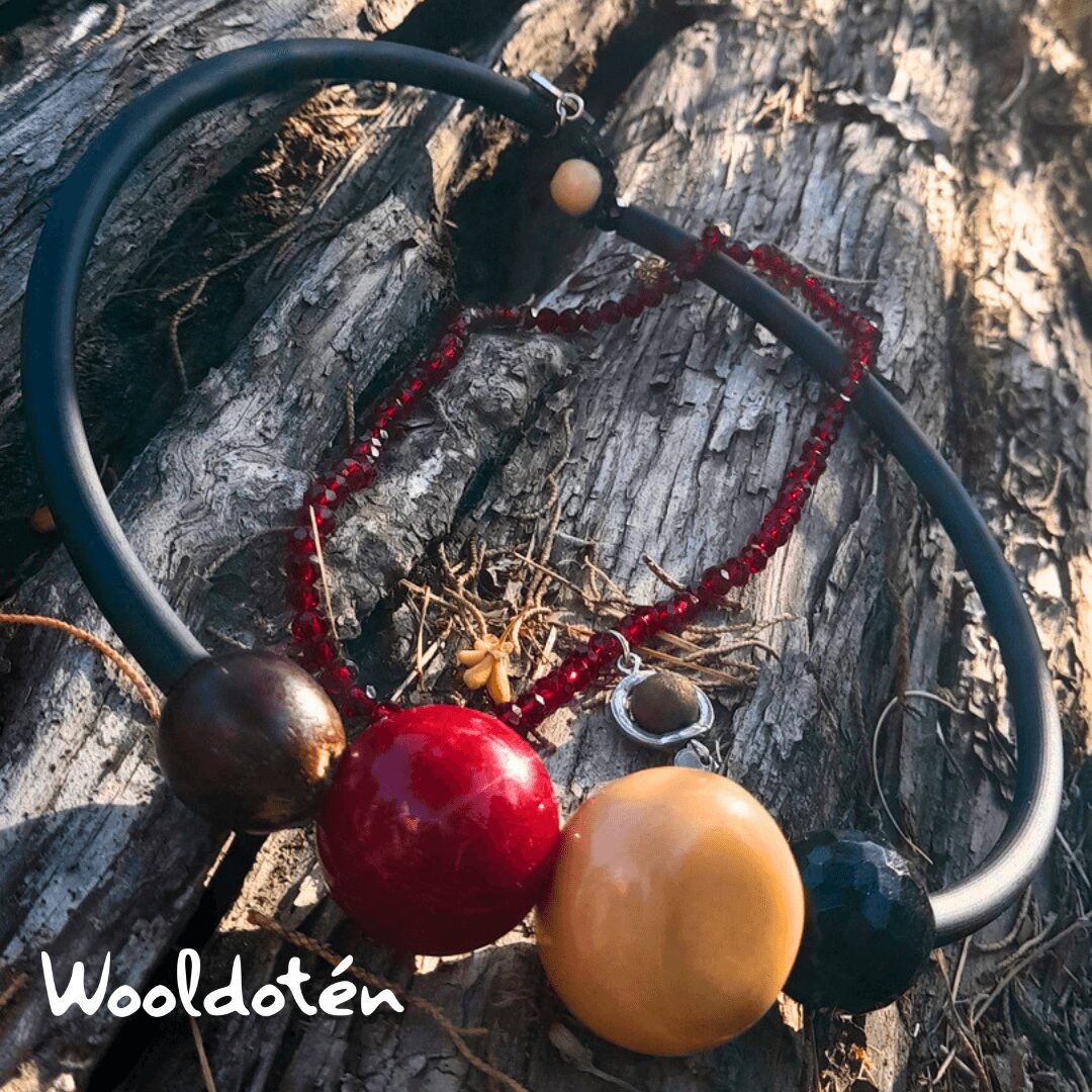Necklace with large red, yellow, and dark beads on a tree trunk, with a black and red string, outdoors.