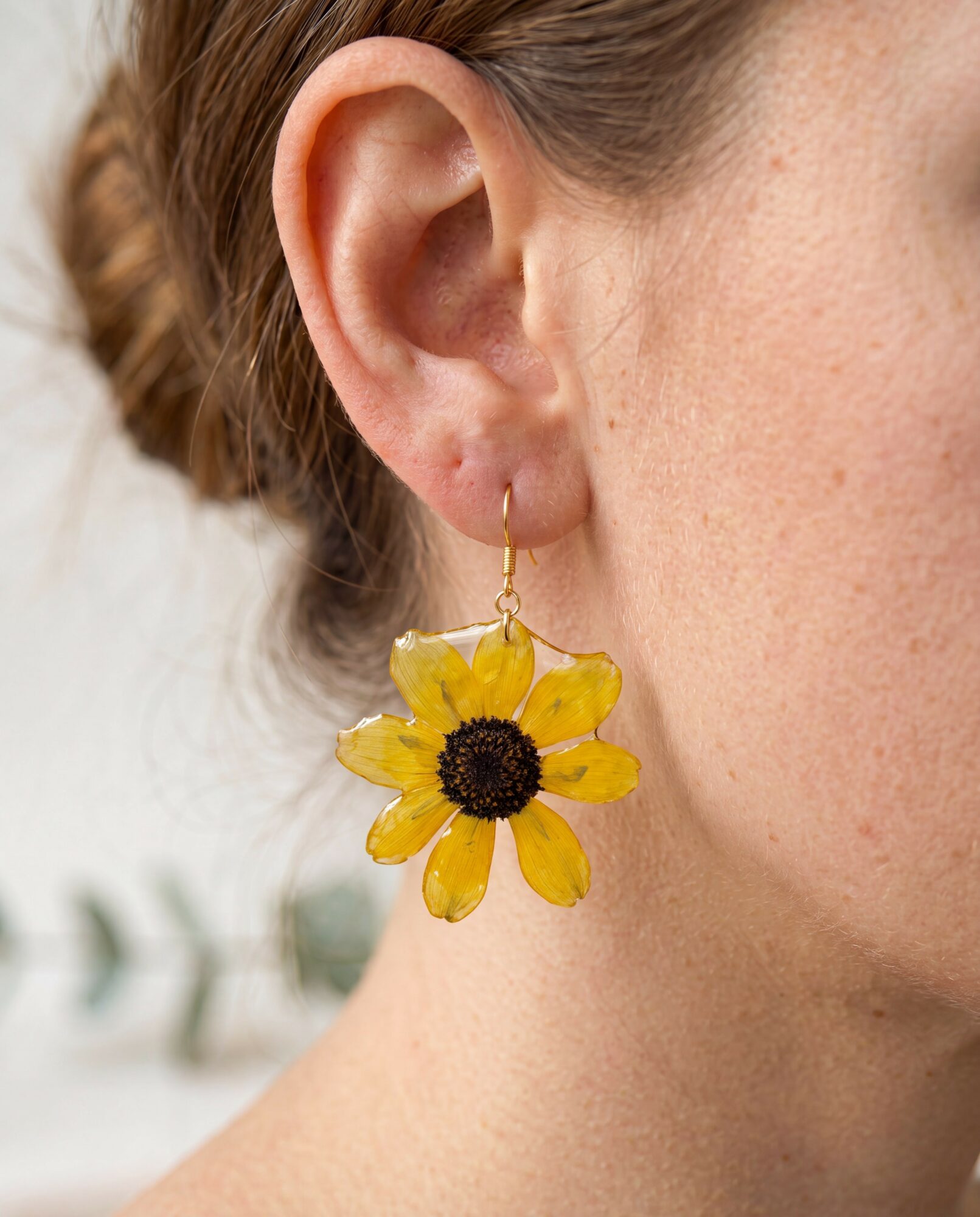 Close-up of a person's ear with a yellow flower earring, part of their face and neck visible.