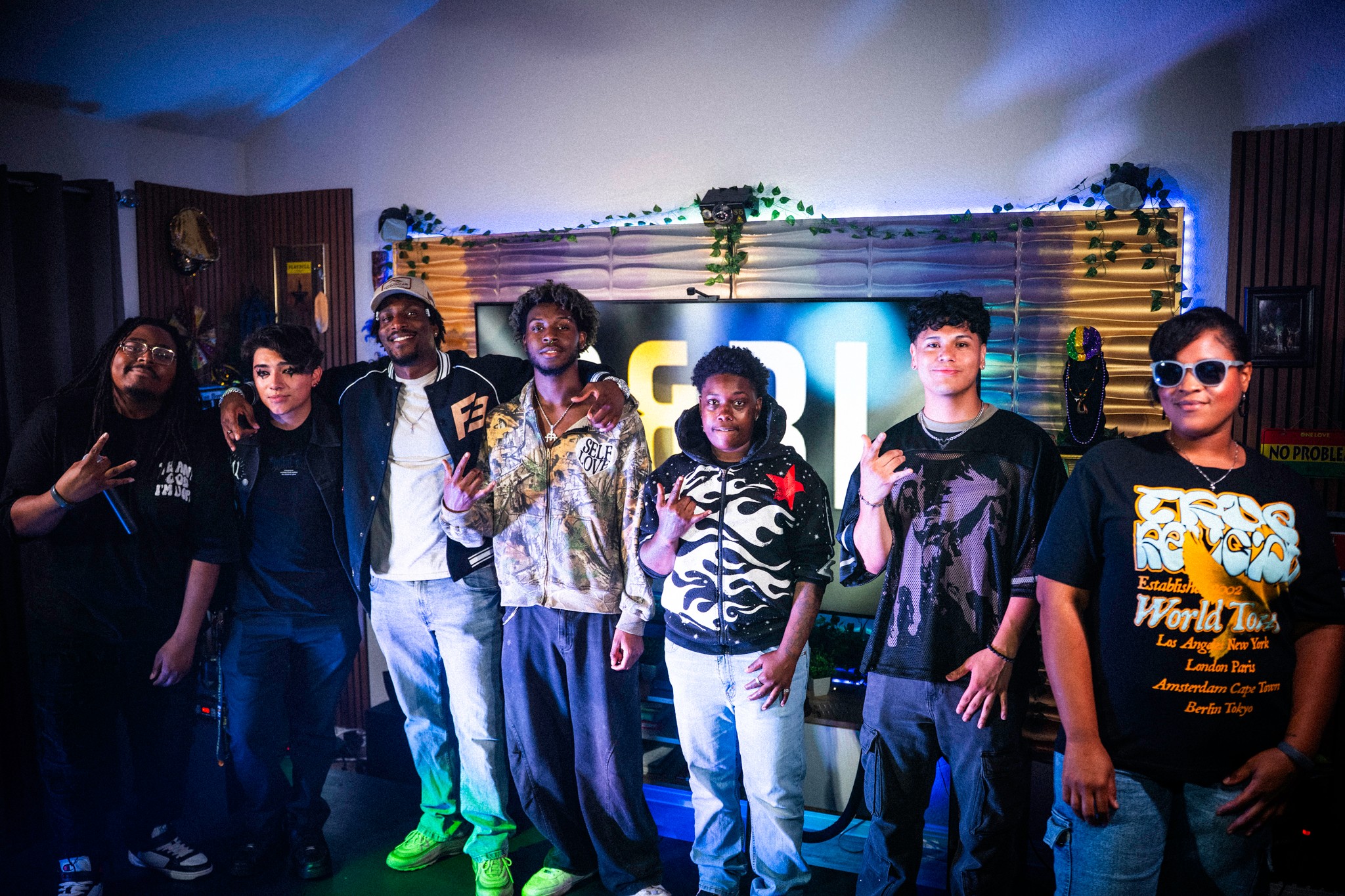 Group of eight people standing in front of a decorated backdrop with lights and plants, posing for a photo.