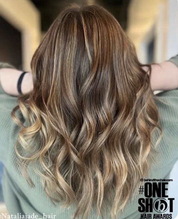 Back view of long, wavy hair with brown and blonde highlights, person wearing a green shirt, arms outstretched.