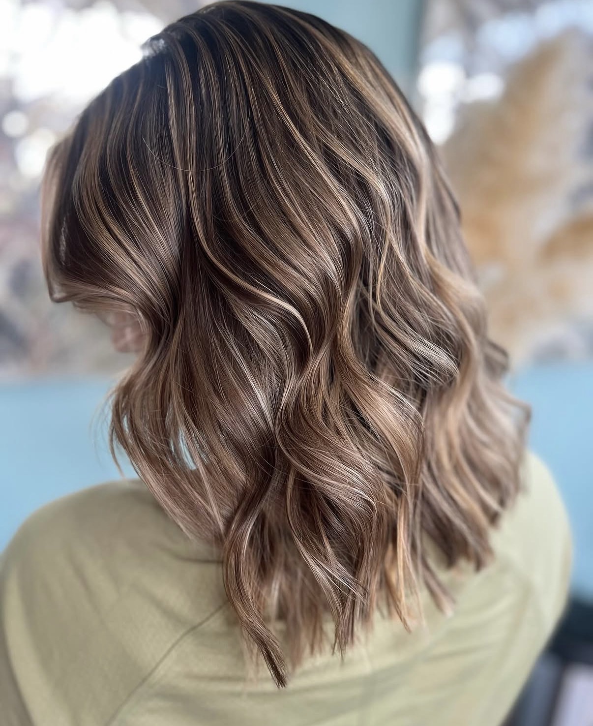 Wavy, shoulder-length hair with highlights, viewed from the back, indoors with blurred background.