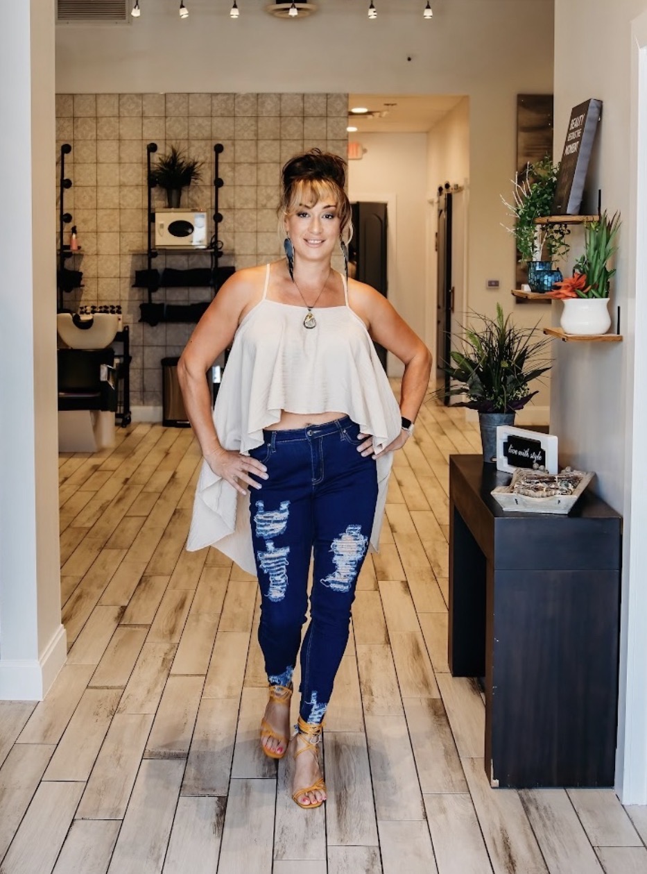 Woman standing indoors with hands on hips, smiling, wearing a white top and ripped jeans, in a modern room.