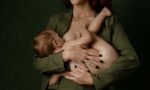 Woman holding a baby and a young child, standing against a dark green background.
