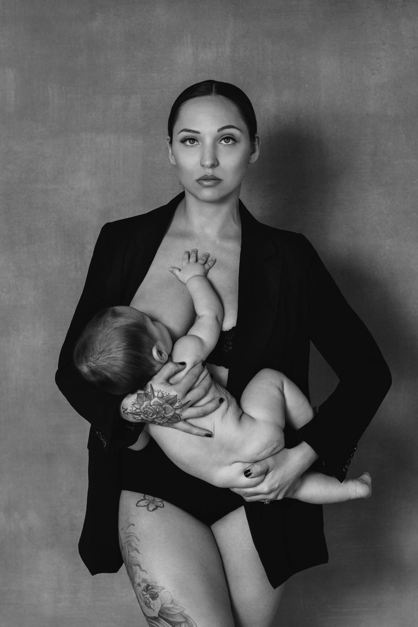 Woman holding a baby, both with tattoos, against a plain background, in black and white.