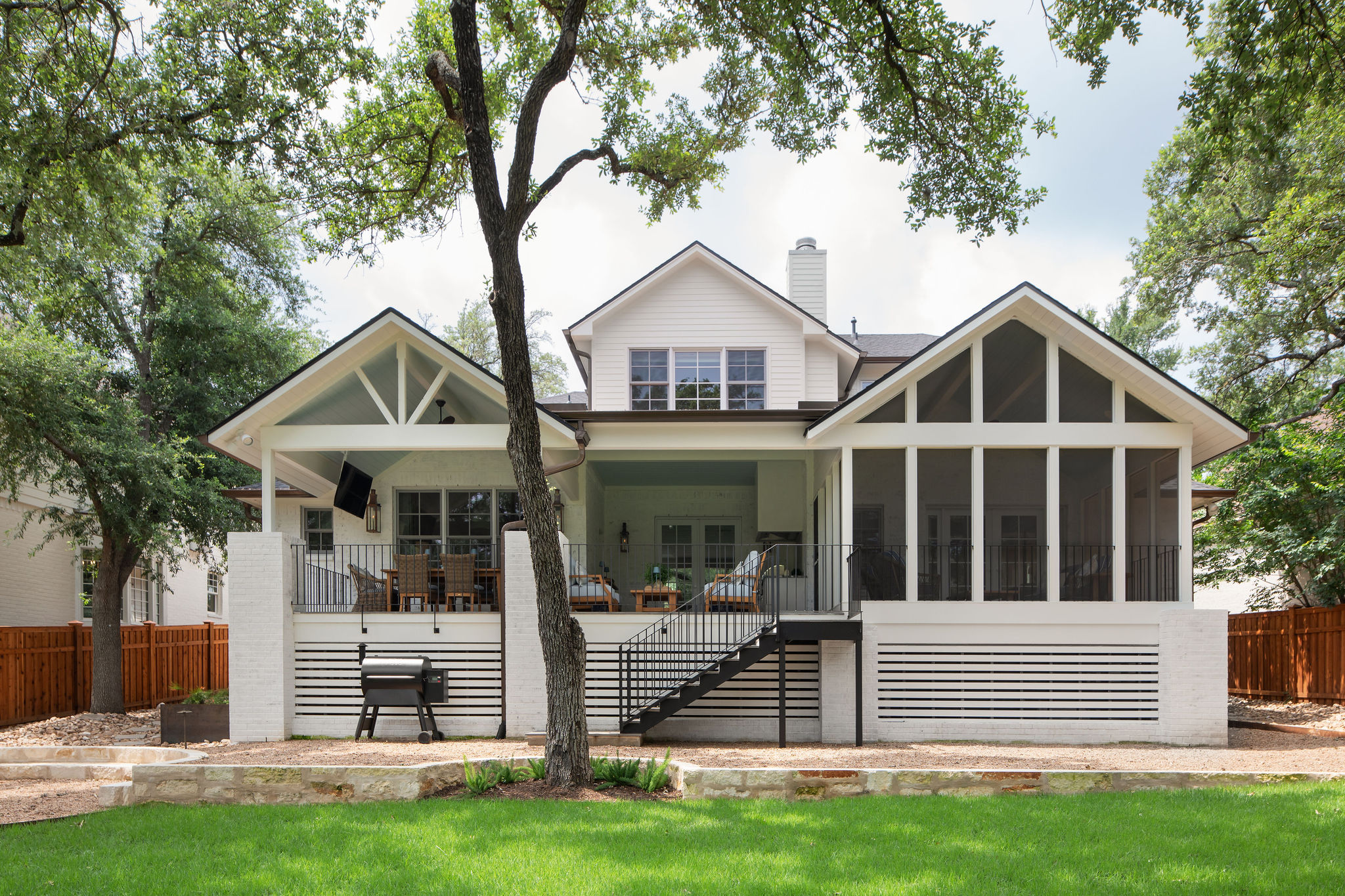 Large house with a porch, multiple windows, and trees in front, under a partly cloudy sky.