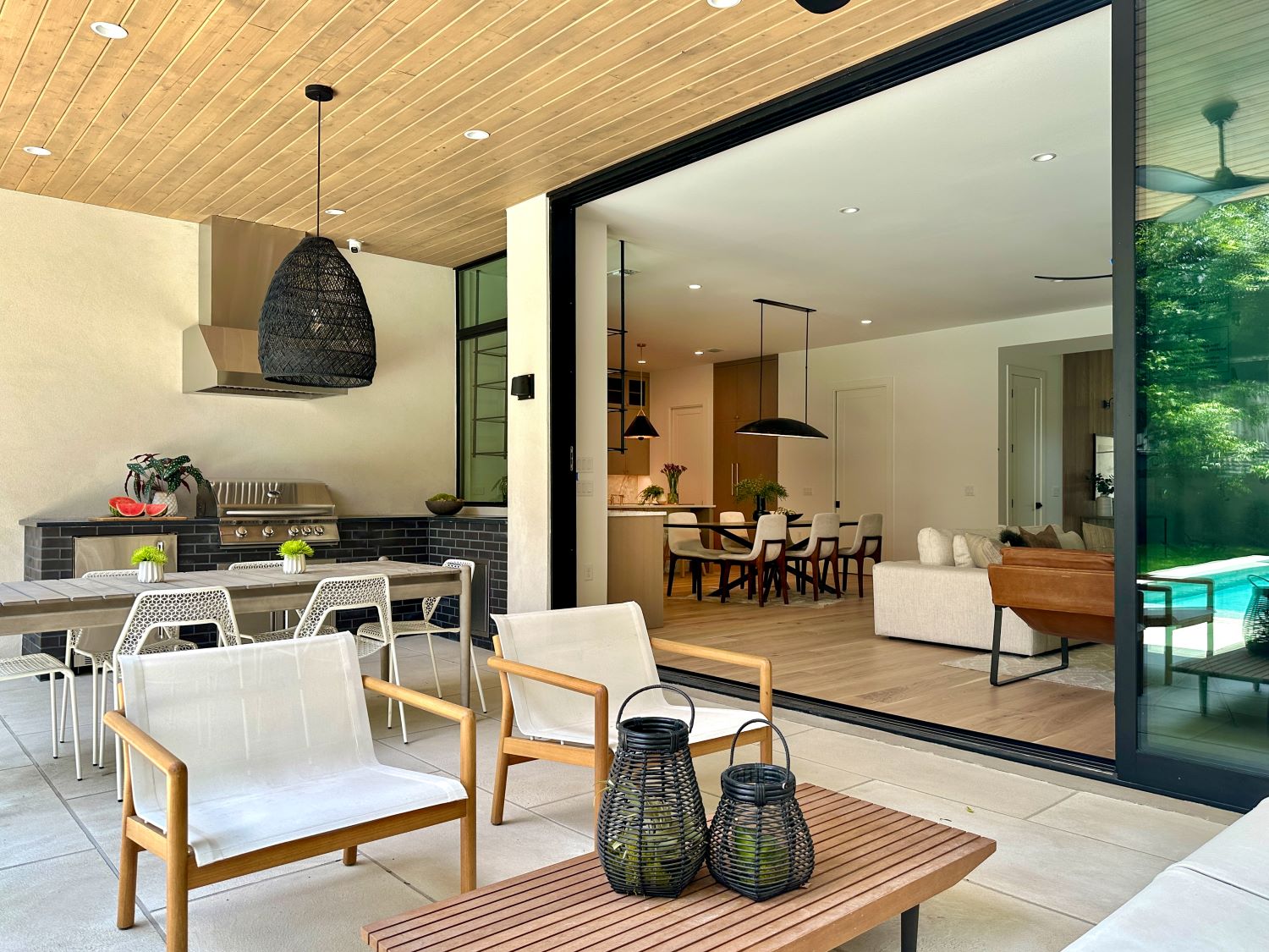 View of a modern living room with large glass sliding doors opening to an outdoor patio, furniture, and decor.