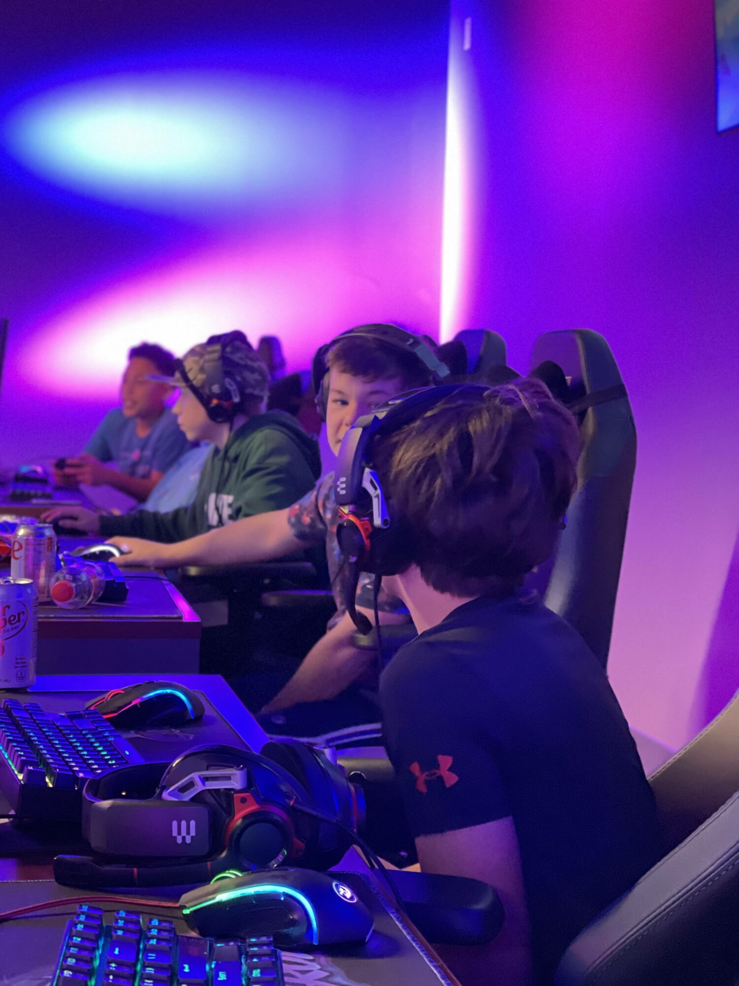 Group of people playing video games in a room with colorful lighting, gaming equipment on the table.
