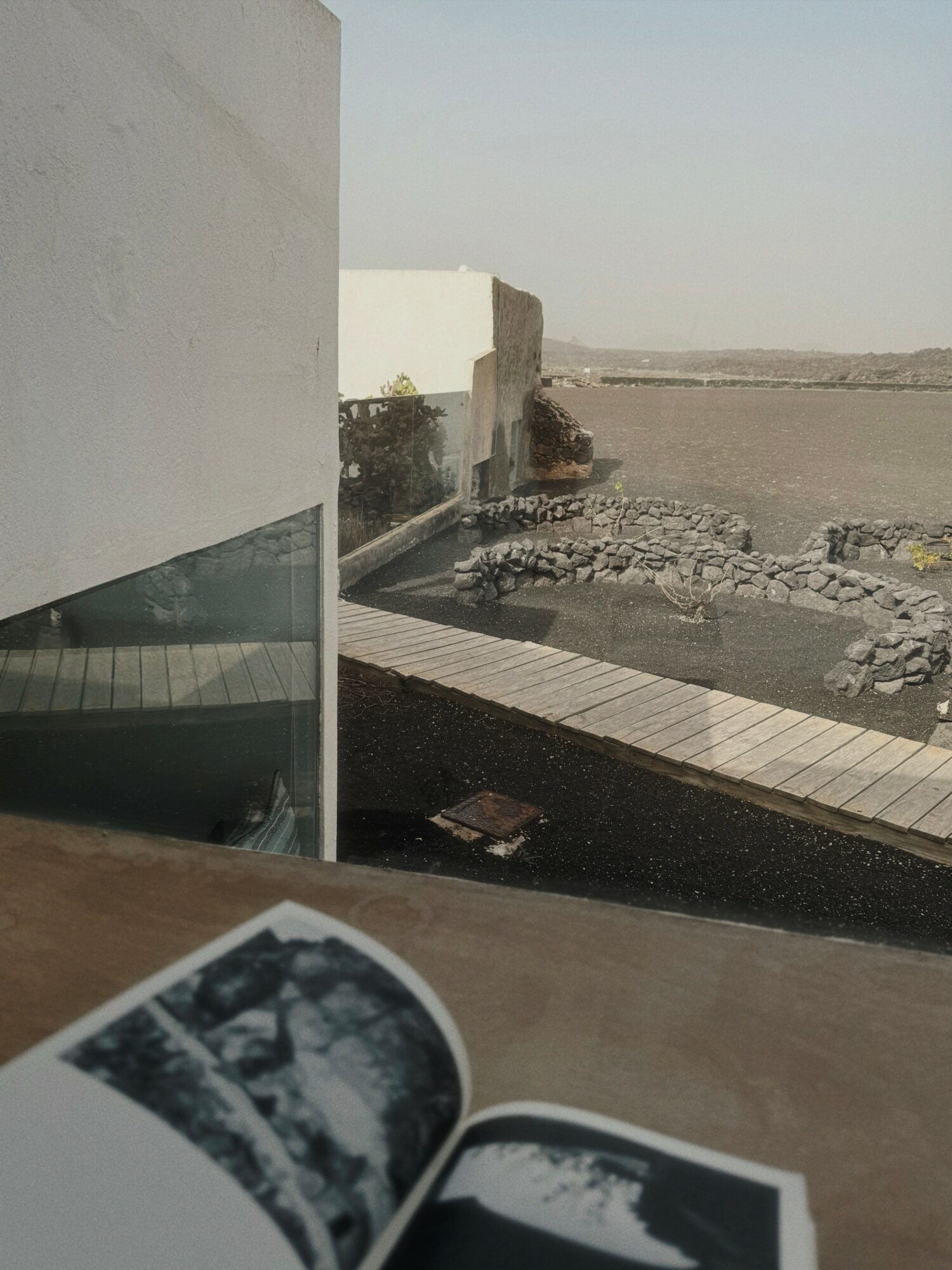 View of a modern building with a glass window, a paved walkway, and a rocky landscape in the distance.