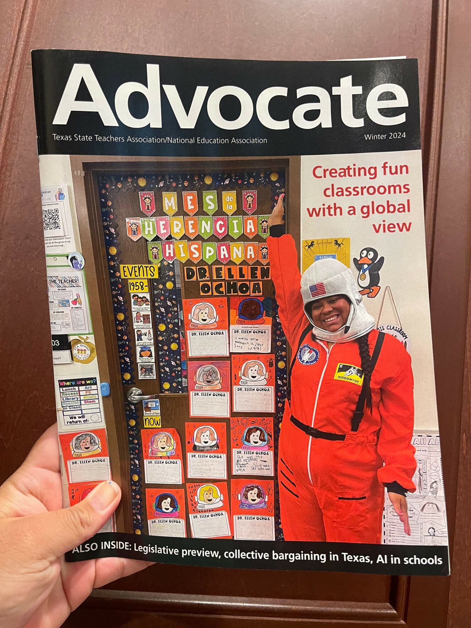 Person holding a magazine titled 'Advocate' with a cover featuring a person in a red jumpsuit and a display of educational materials.