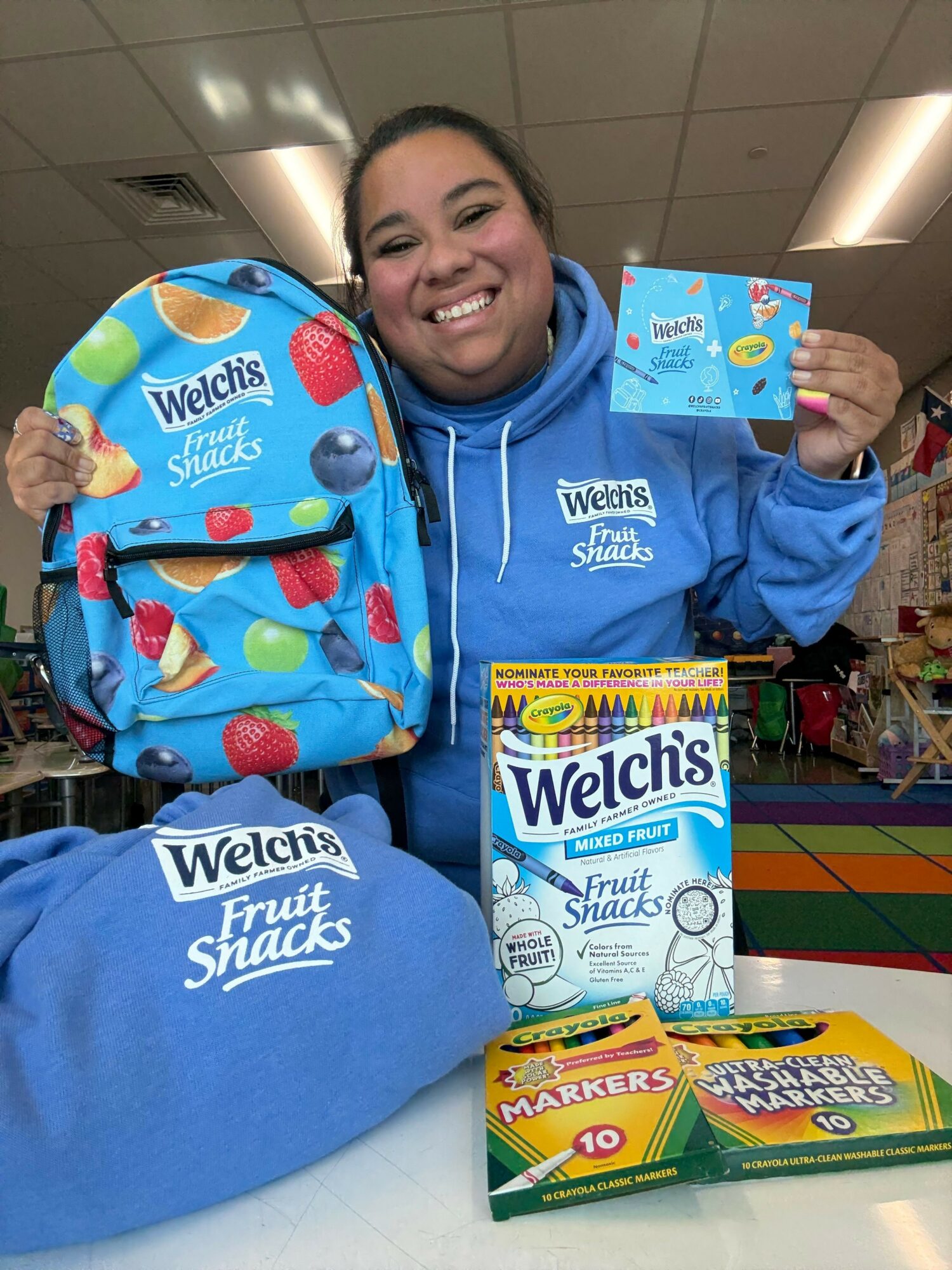 Smiling girl holding a card, surrounded by Welch's juice boxes and a blue Welch's tote bag, in a store.