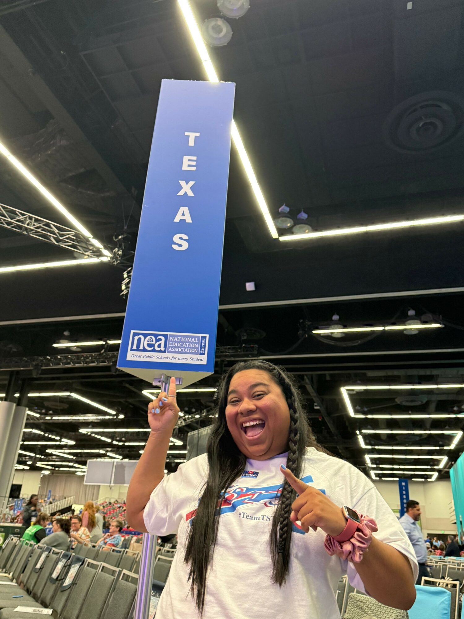 Young girl with long dark hair and a white shirt points at a Texas sign inside a store.
