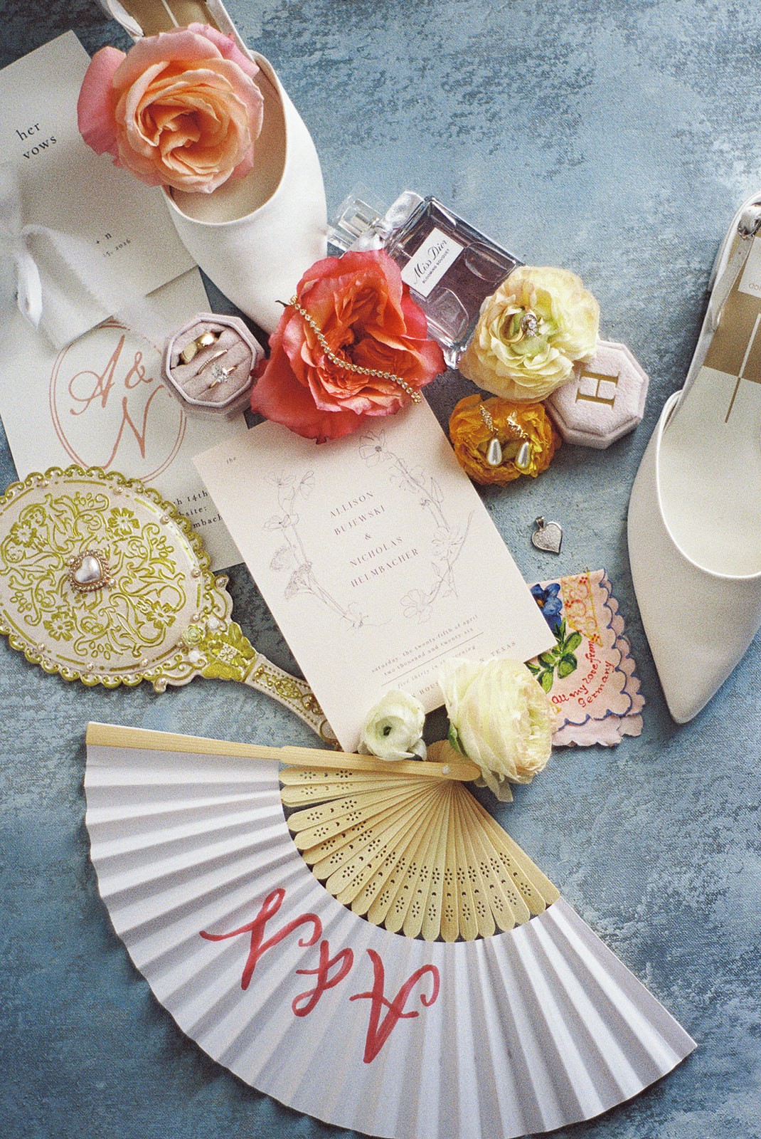 Decorative fan, flowers, perfume bottles, and jewelry on a blue surface with a white shoe nearby.