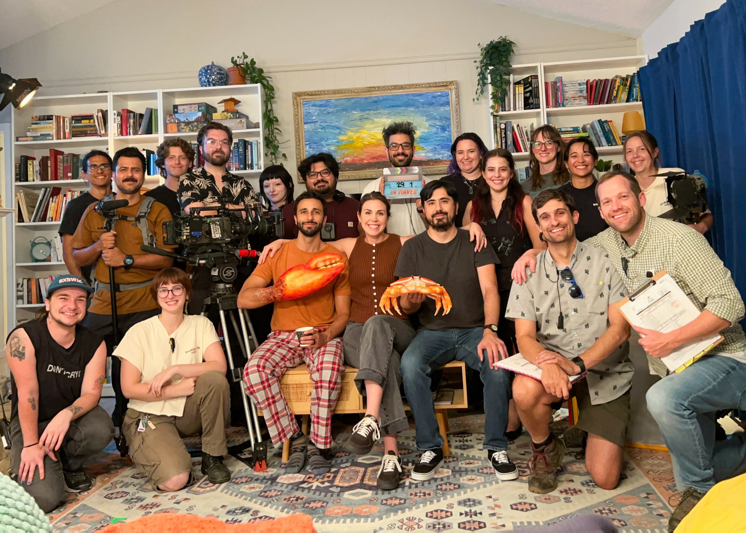 Group of 16 people in a room with bookshelves, some holding books or musical instruments, smiling for a photo.