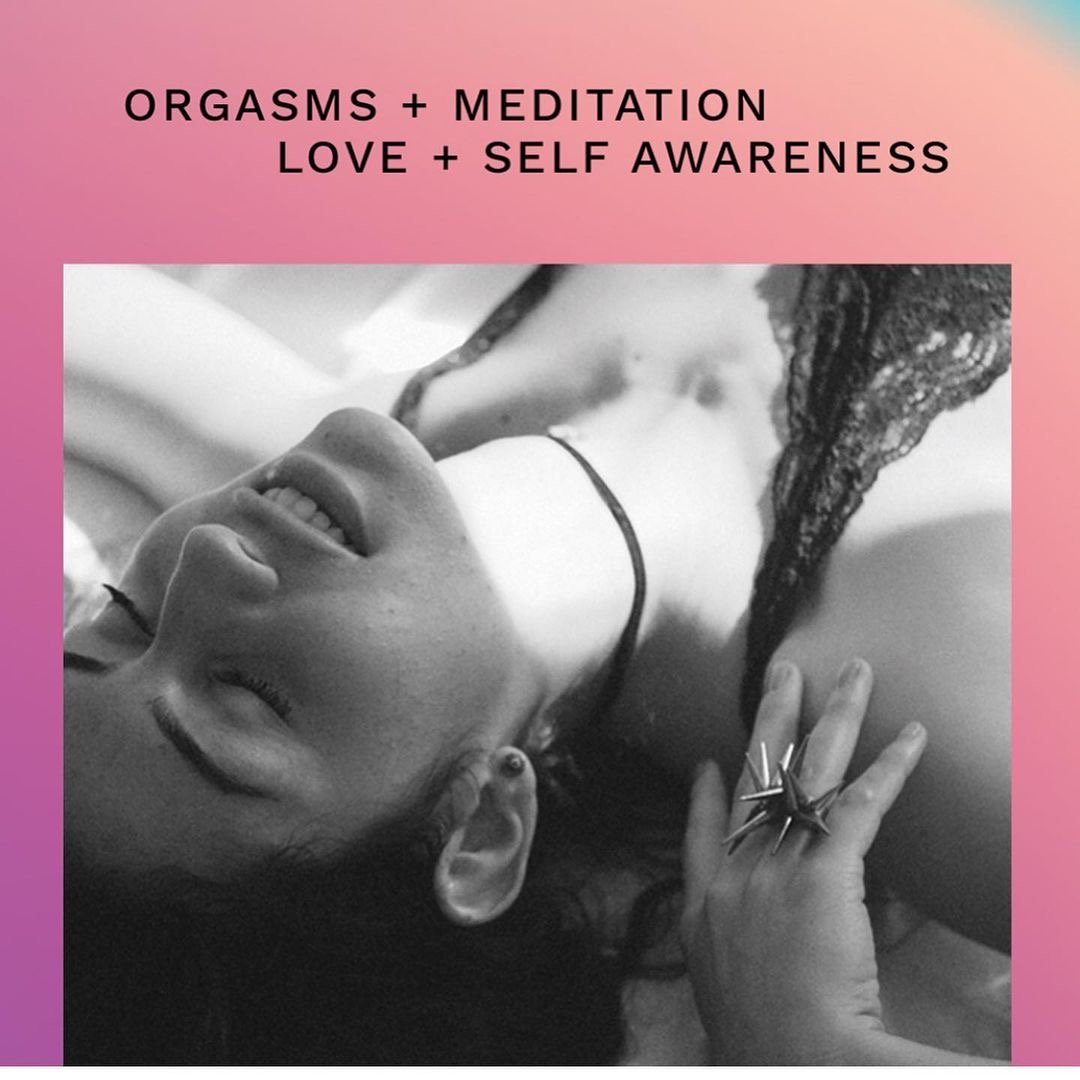 Black and white photo of a woman lying down with eyes closed, smiling, and hand near face, on pink background.