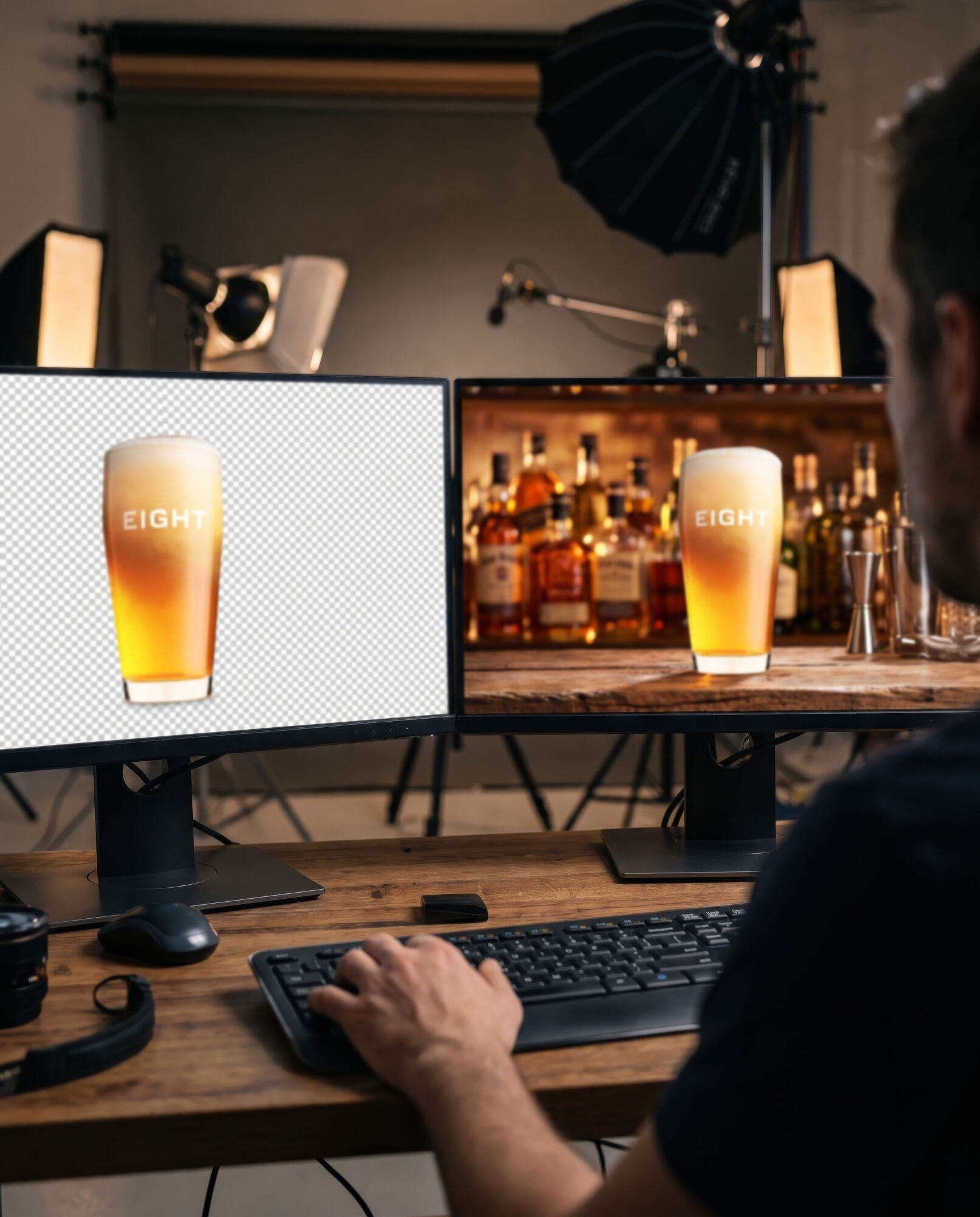 Person working at a desk with two monitors displaying a beer glass, in a studio setting with lighting equipment