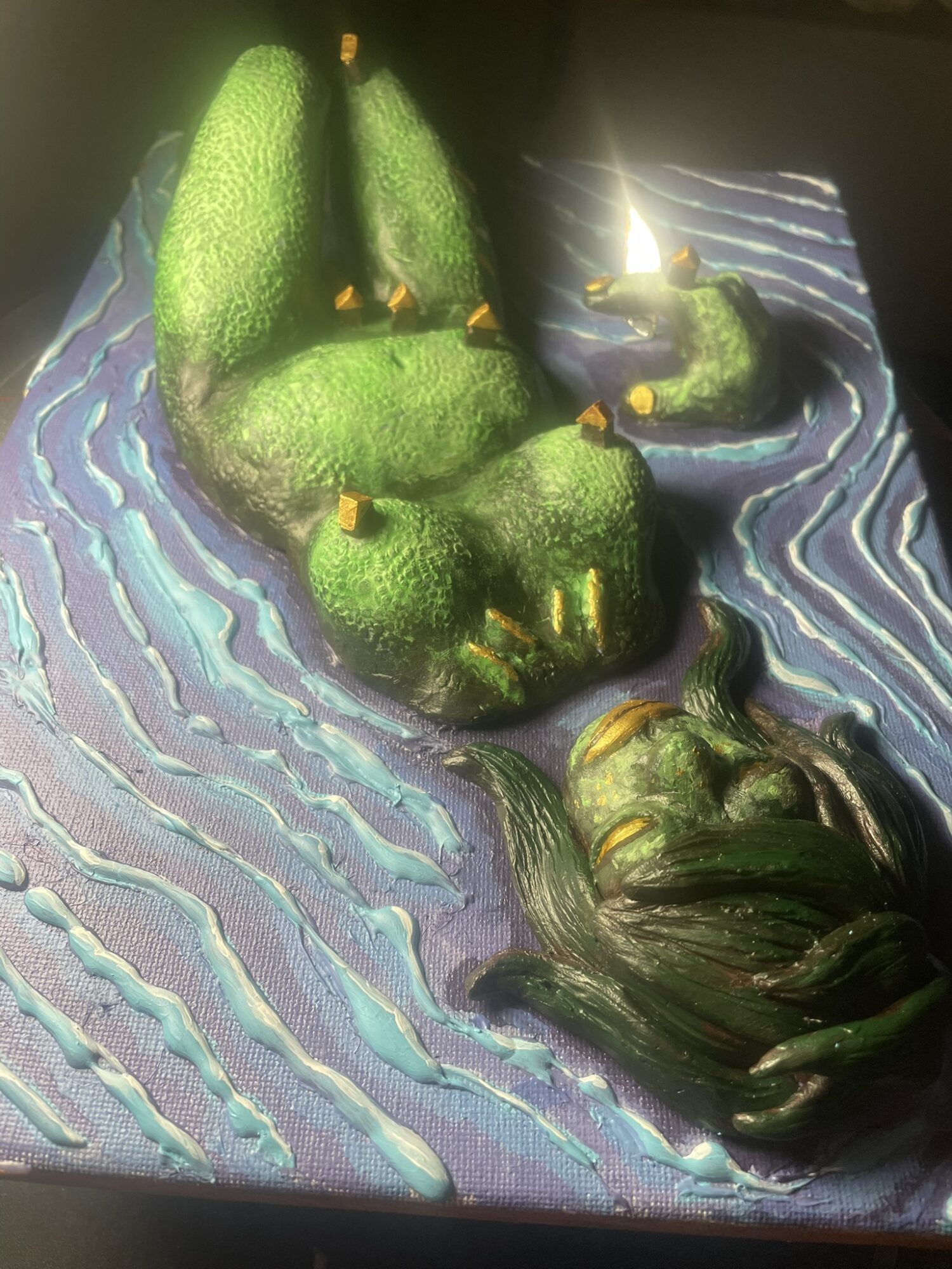 A cake resembling a green dragon with wings, lying on a textured blue and purple surface, with a dark background.