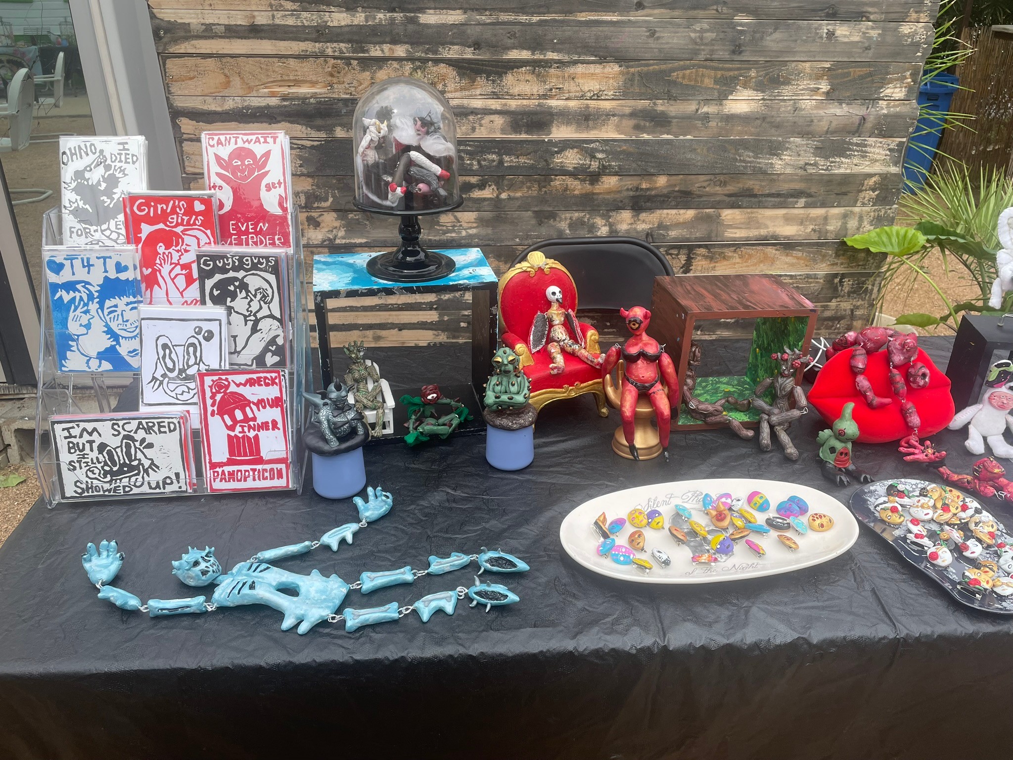 Table with various decorative items, toys, and artwork, including a skeleton, plush toys, and colorful jewelry displays.