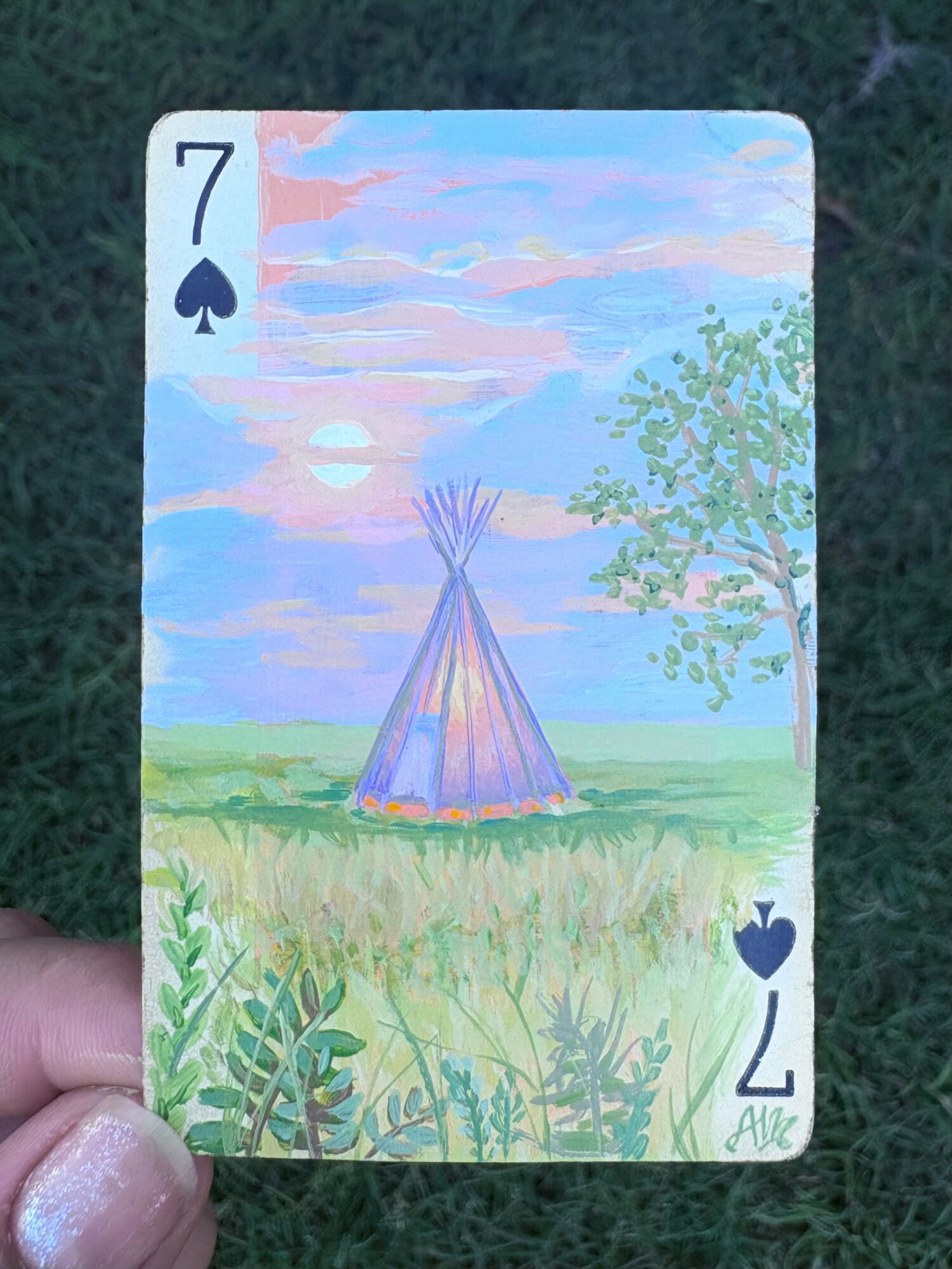 A painted card showing a teepee in a grassy field with a tree and sky, labeled 7 of spades.
