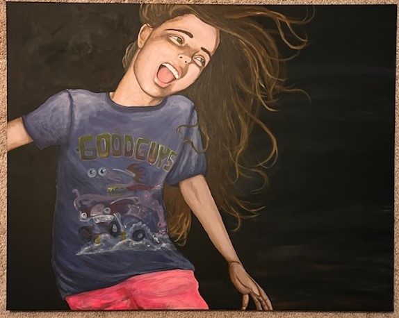 Young woman with long hair, wearing a graphic T-shirt and pink shorts, smiling and sticking out her tongue.