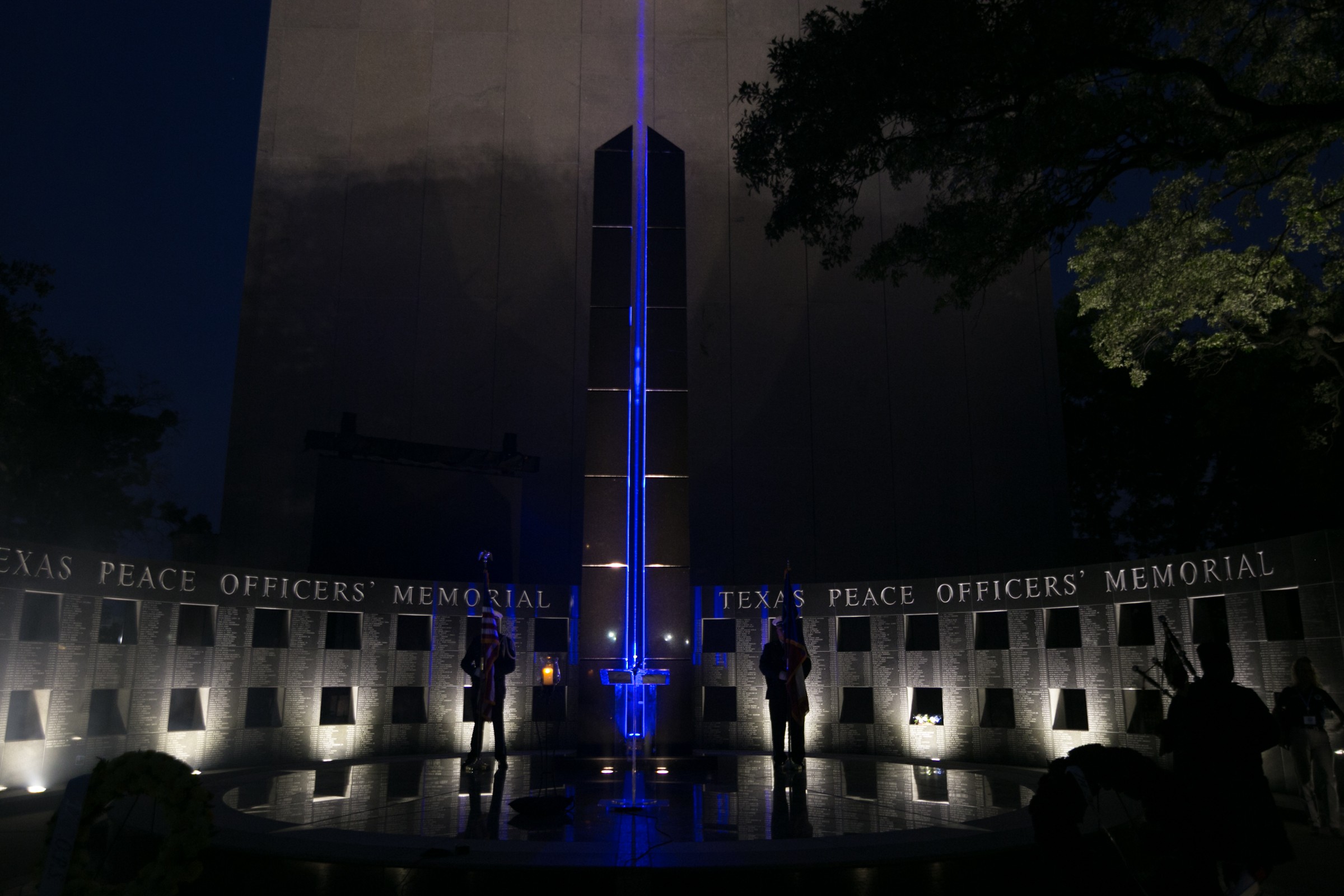 Nighttime scene of Texas Peace Officers Memorial with illuminated wall and people standing nearby.