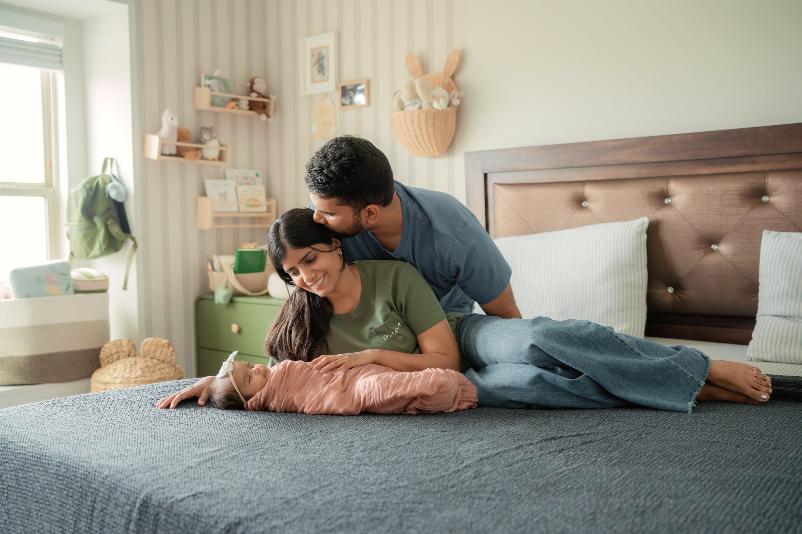 Two people on a bed in a bedroom, one sitting and the other leaning over, with a window and shelves in the background.