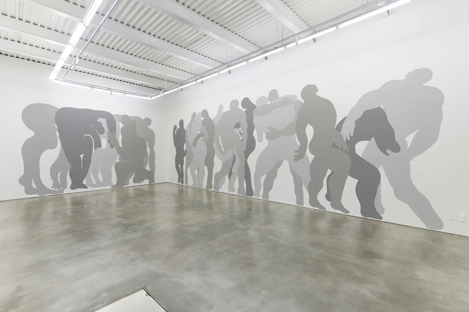 Silhouettes of people walking and standing along a white wall in an art gallery.