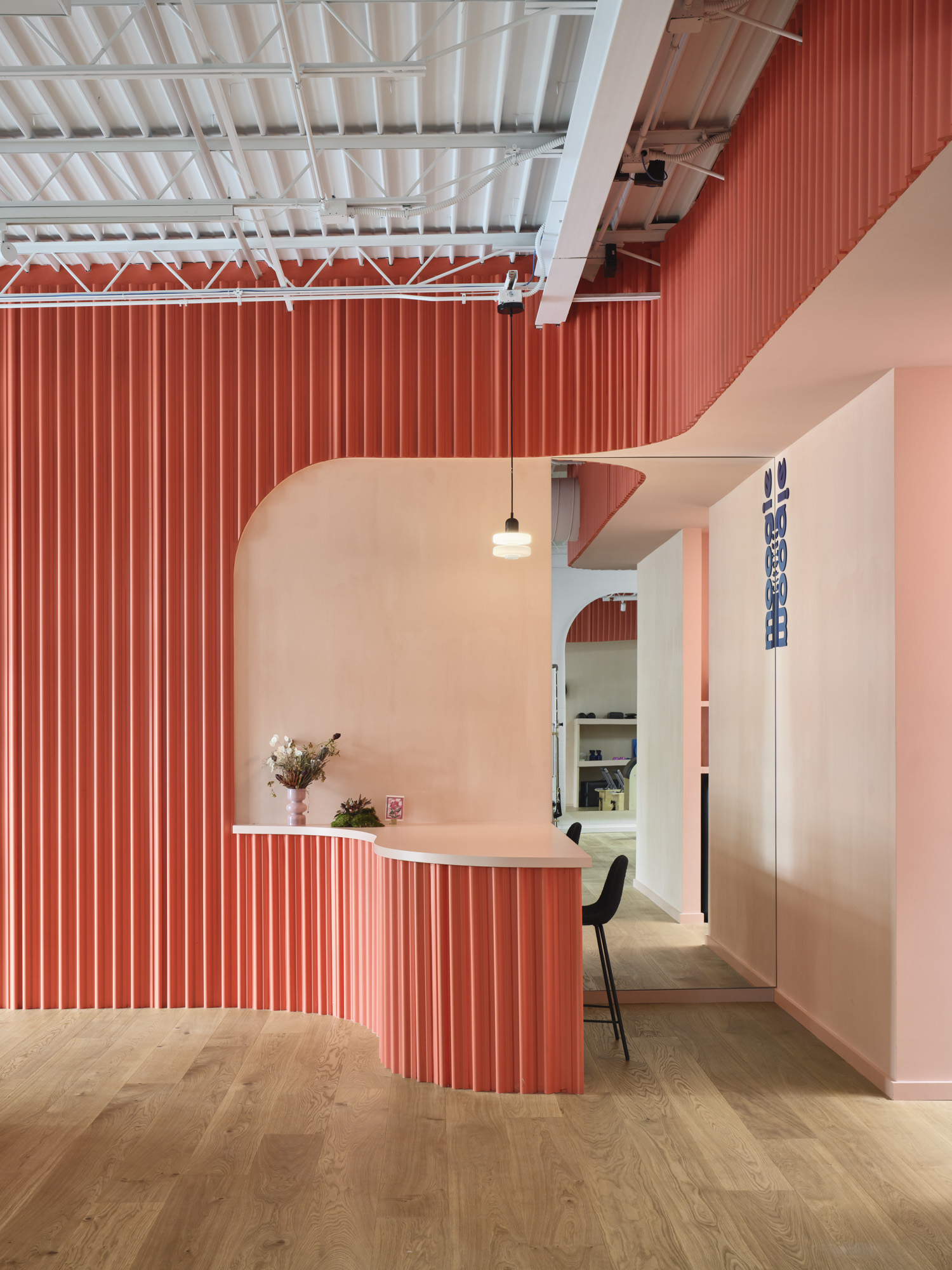Interior space with red vertical striped wall, white curved counter, hanging light, and a black chair, with wooden floor.