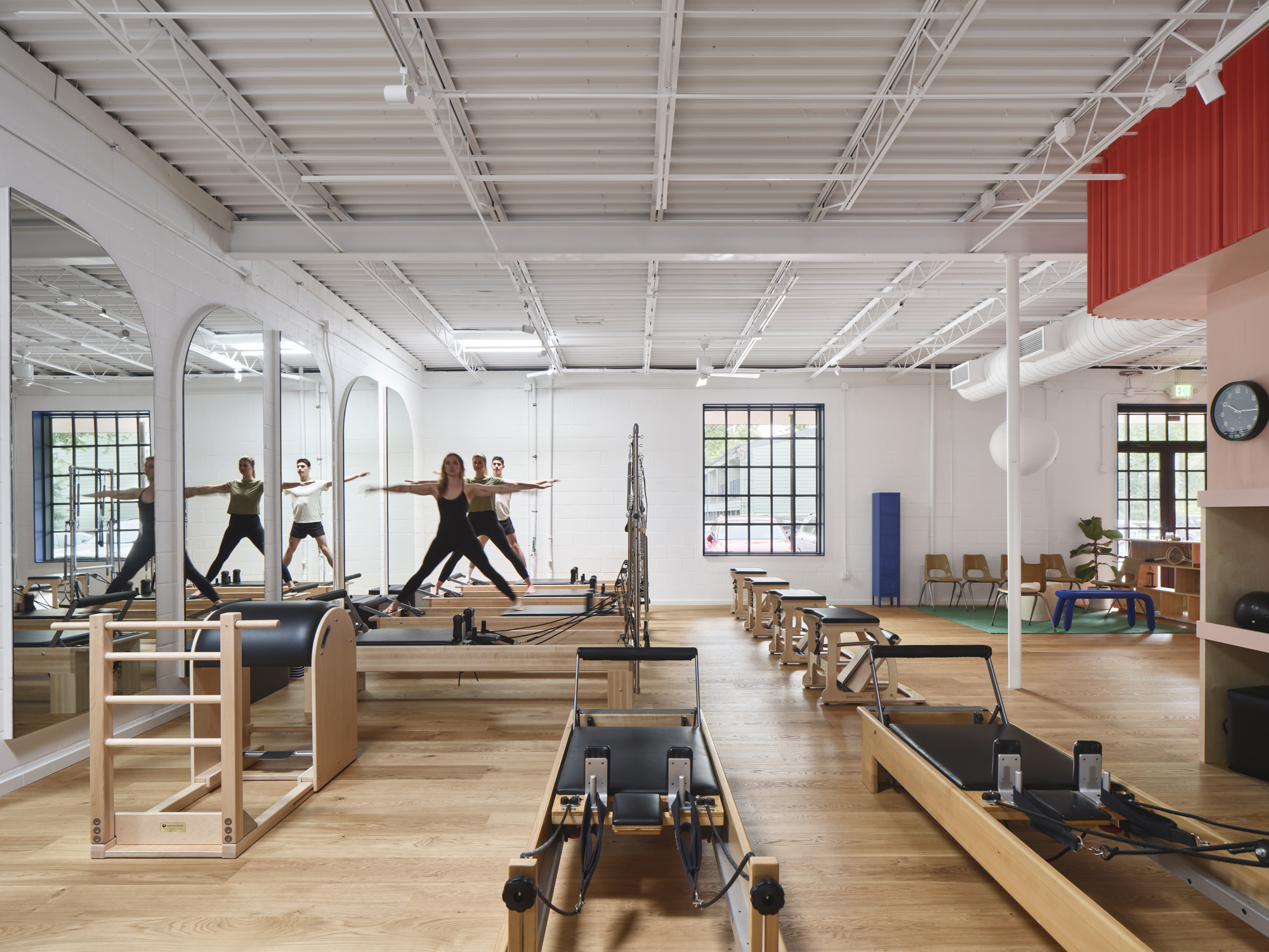 Group of people practicing Pilates on reformer machines in a spacious, well-lit fitness studio with large windows.