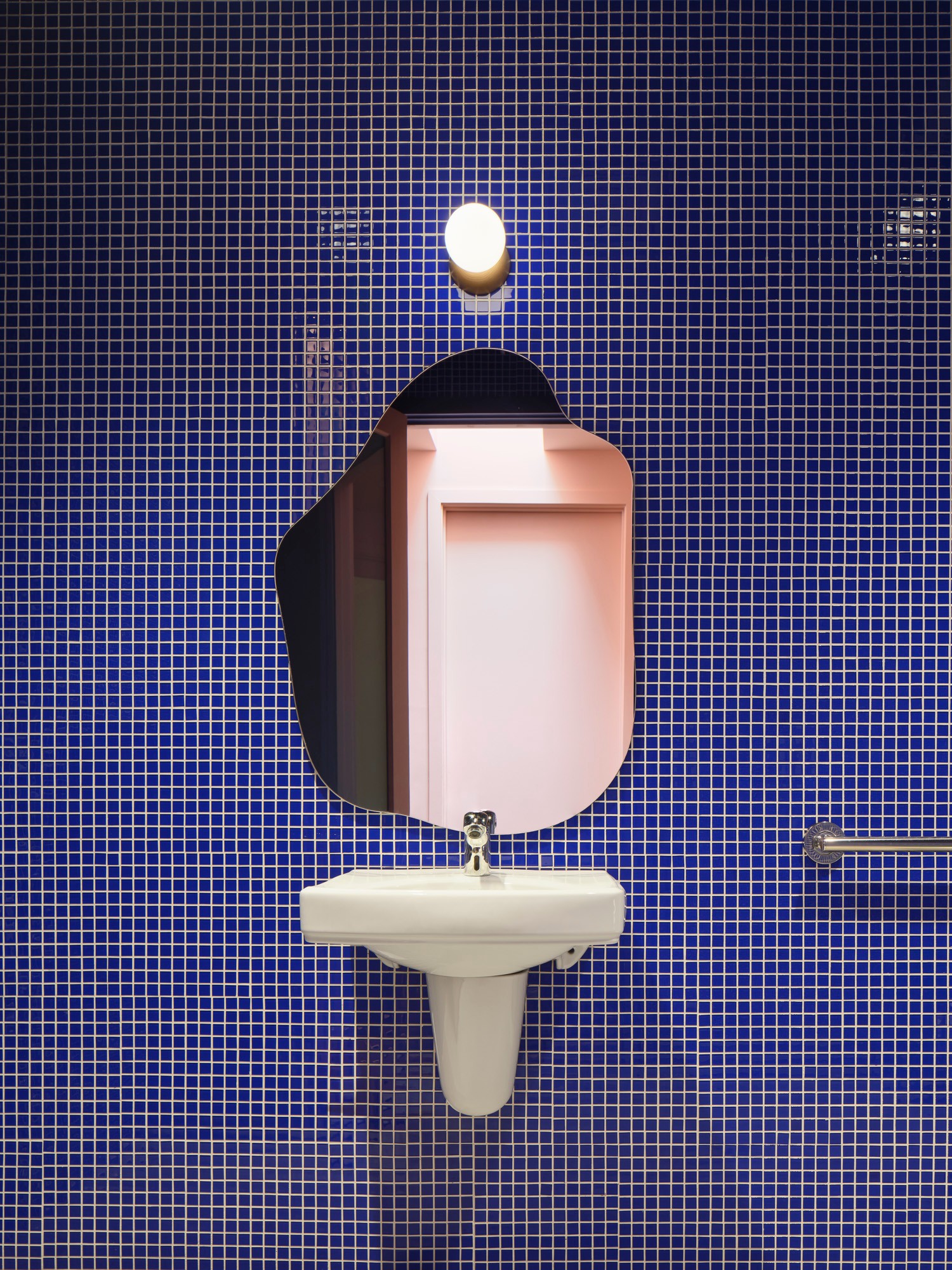 Pink mirror above a white sink against a blue tiled wall, with a soap dispenser and a towel bar.