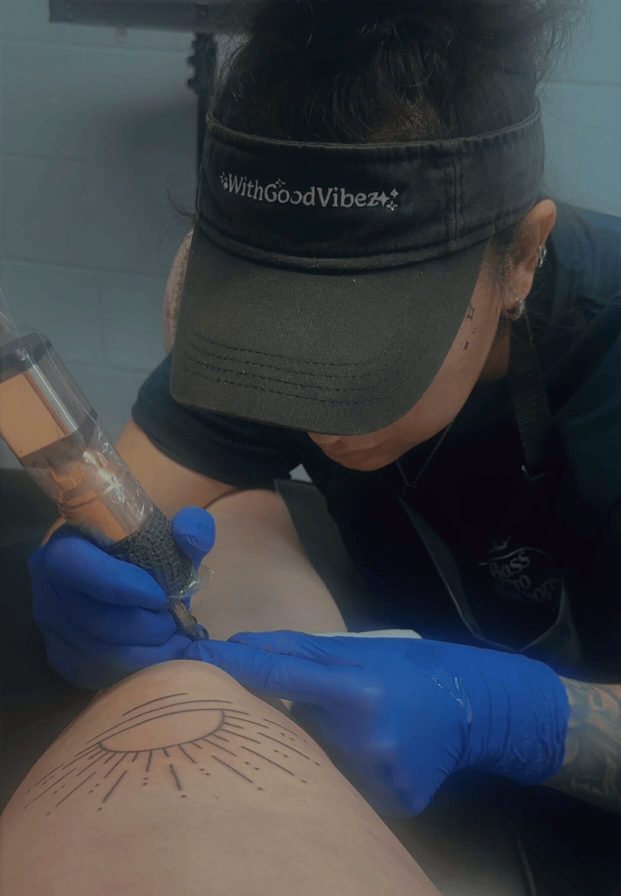 Person wearing a visor and gloves tattooing a design on a person's skin.