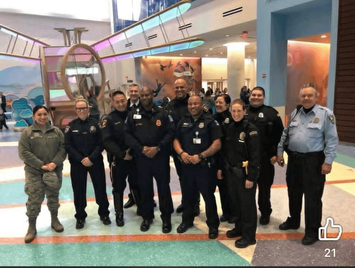 Group of police officers and a person in military uniform standing indoors, colorful background, some smiling, in a public space.
