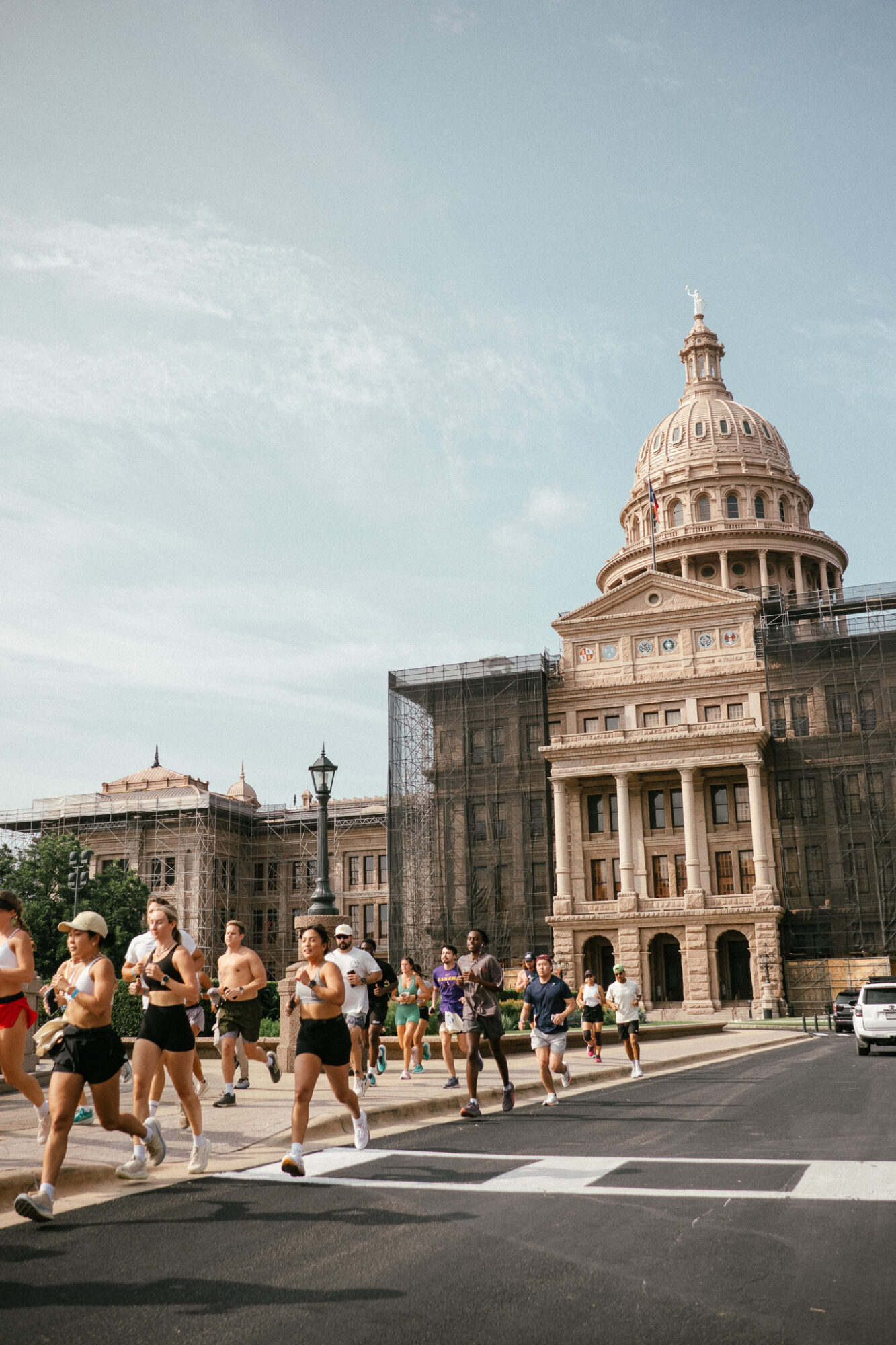 People crossing a street in front of a historic building with a large dome, under a partly cloudy sky.